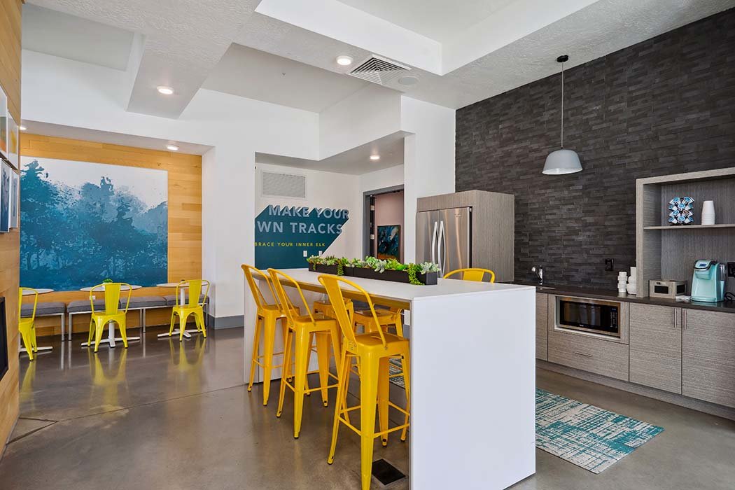 Modern kitchen and dining area with yellow chairs, a white kitchen island, dark accent wall, and minimalist decor.