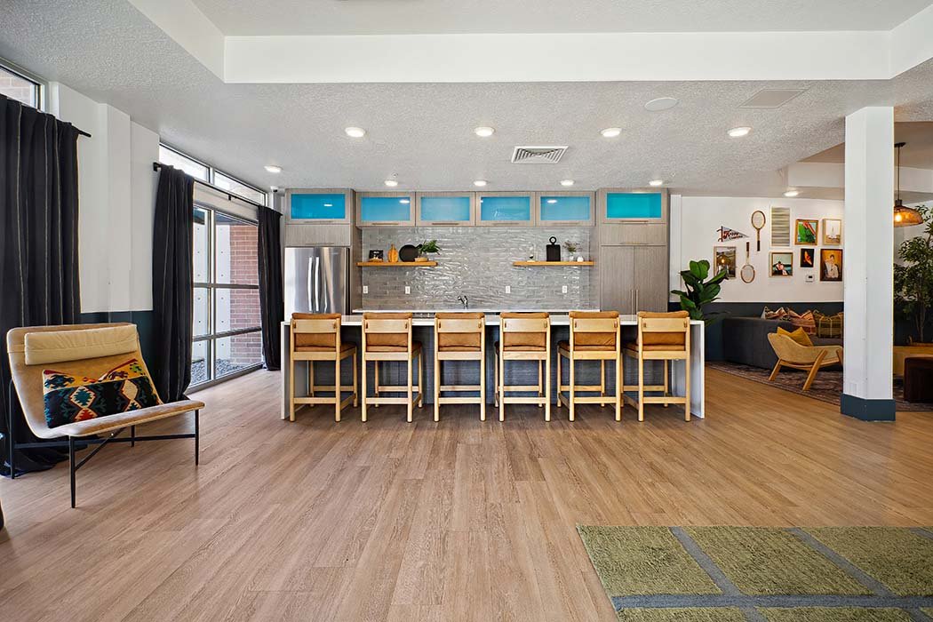 Modern open-concept kitchen and living area with bar seating, wood flooring, black curtains, and wall art.