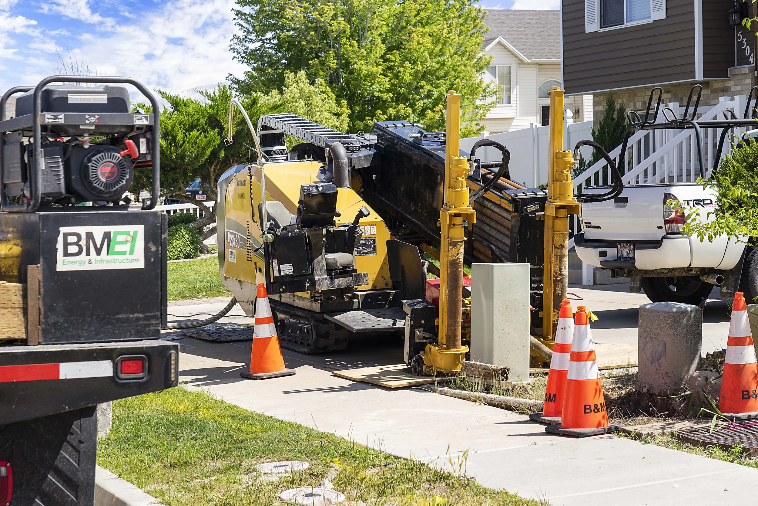 Construction site in front of a residential house with construction equipment, orange cones, and a truck nearby.