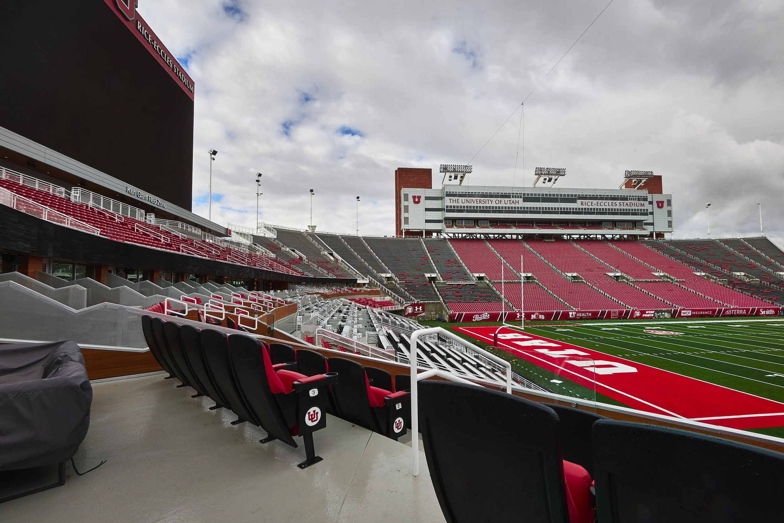 Empty football stadium with red and black seats, view of the field, and a large scoreboard.