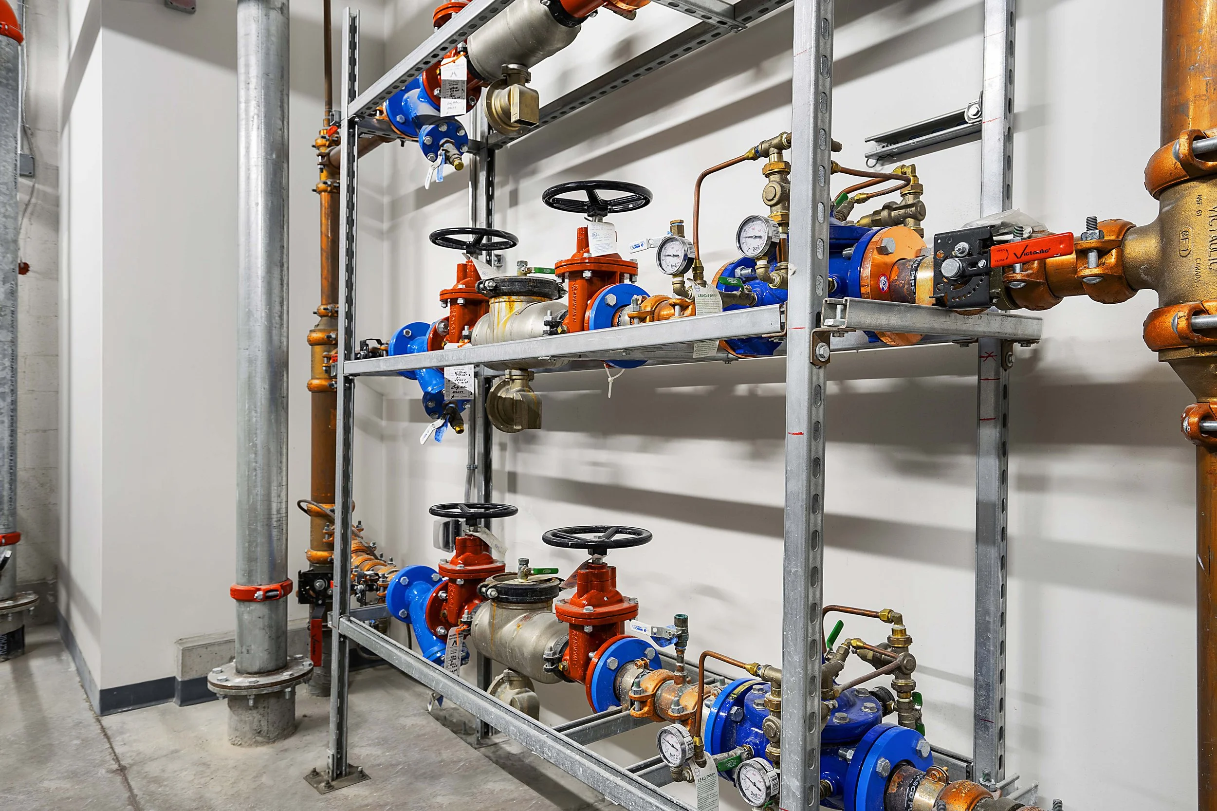 Industrial pipes, valves, and gauges mounted on a metal frame in a mechanical room.
