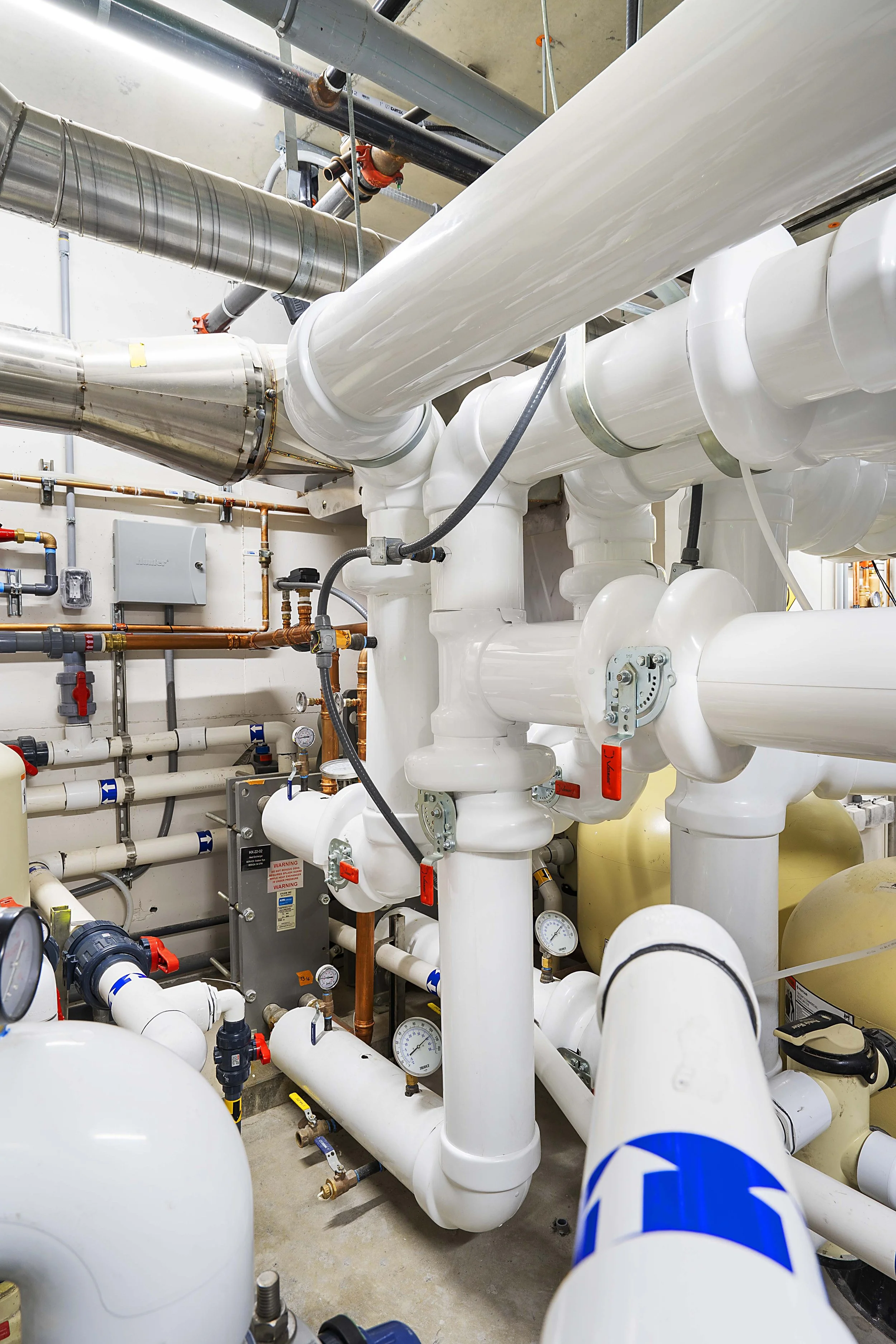 A complex system of white and metallic pipes, valves, and gauges in an industrial setting, possibly part of a plumbing or HVAC system.
