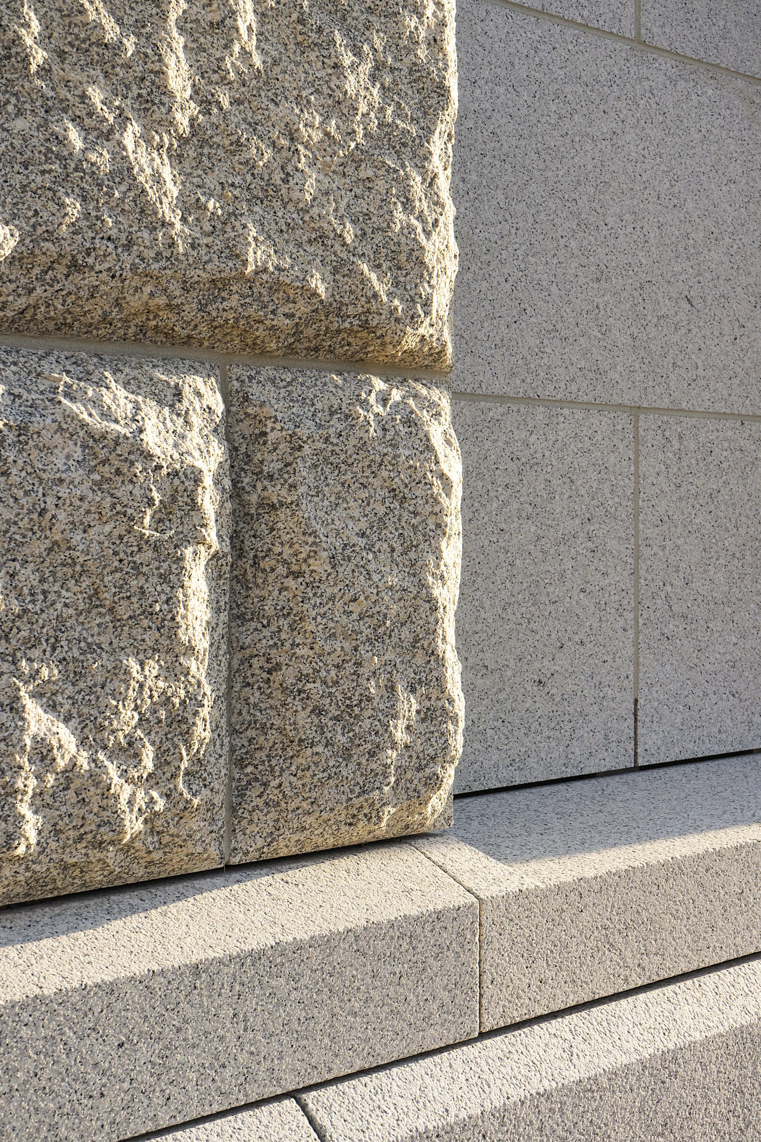 Close-up of a corner of a building showing textured and smooth stone blocks in shades of beige and light gray.