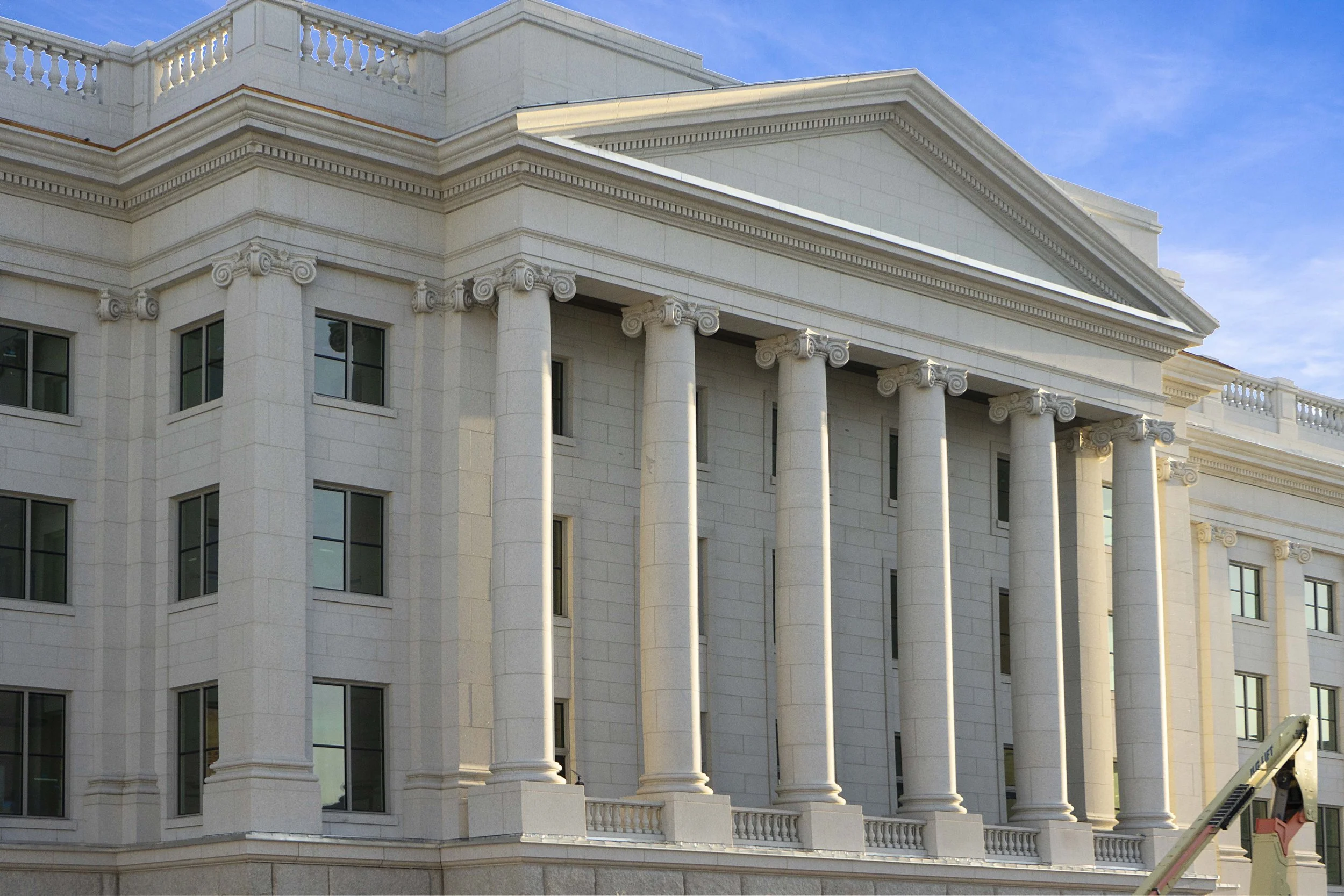 A large, white neoclassical building with tall columns and a triangular pediment, under a blue sky.