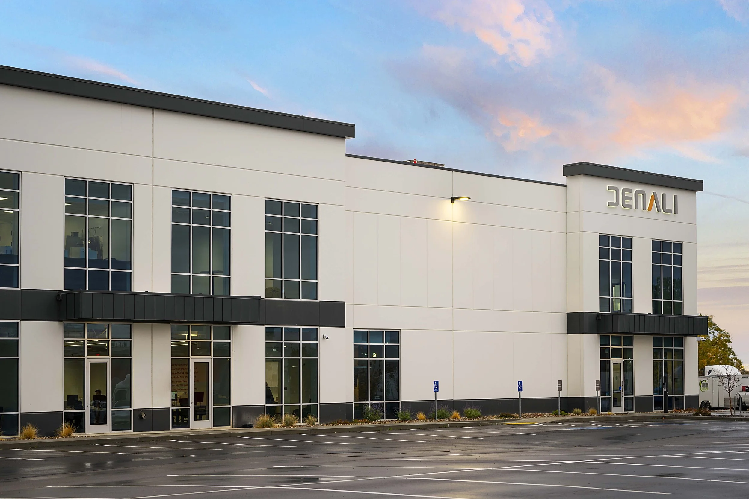 Modern commercial building with large windows and signage, exterior view at dusk with a mostly empty parking lot.