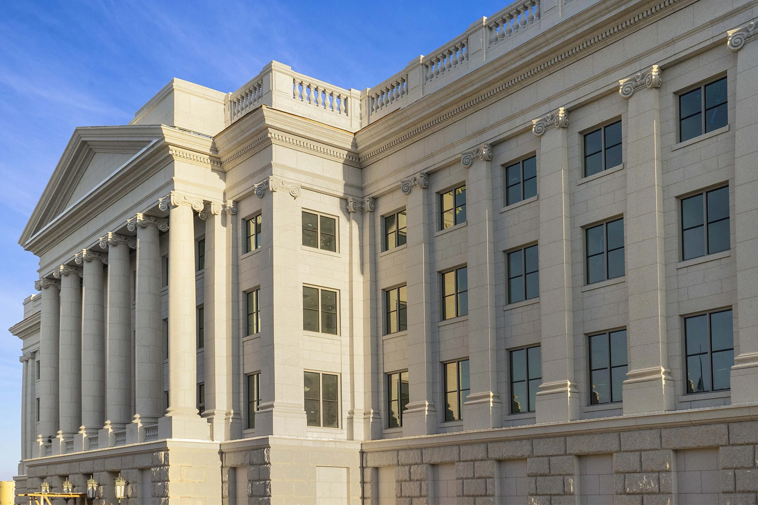 Exterior of a neoclassical-style building with tall columns, decorative balustrades, and multiple windows, under a clear blue sky.