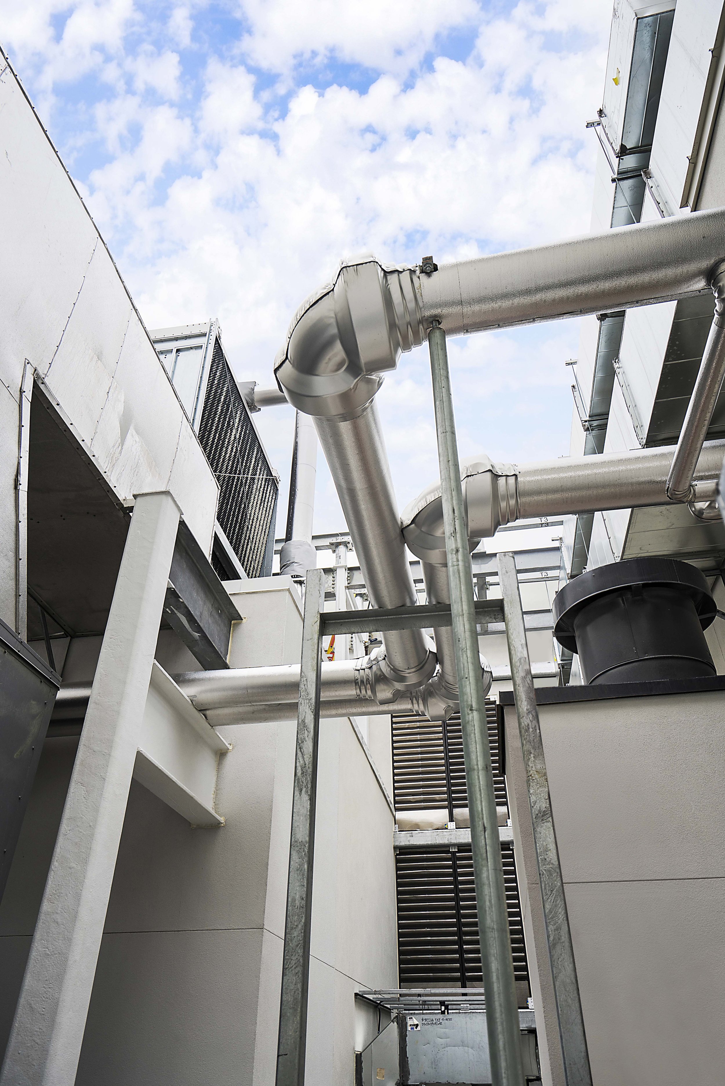 View of rooftop with metal pipes, vents, and air conditioning units against a partly cloudy sky.