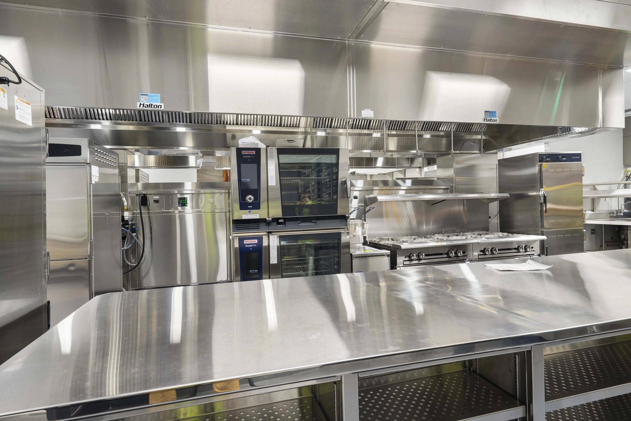 Commercial stainless steel kitchen with stove, ovens, and work surfaces.