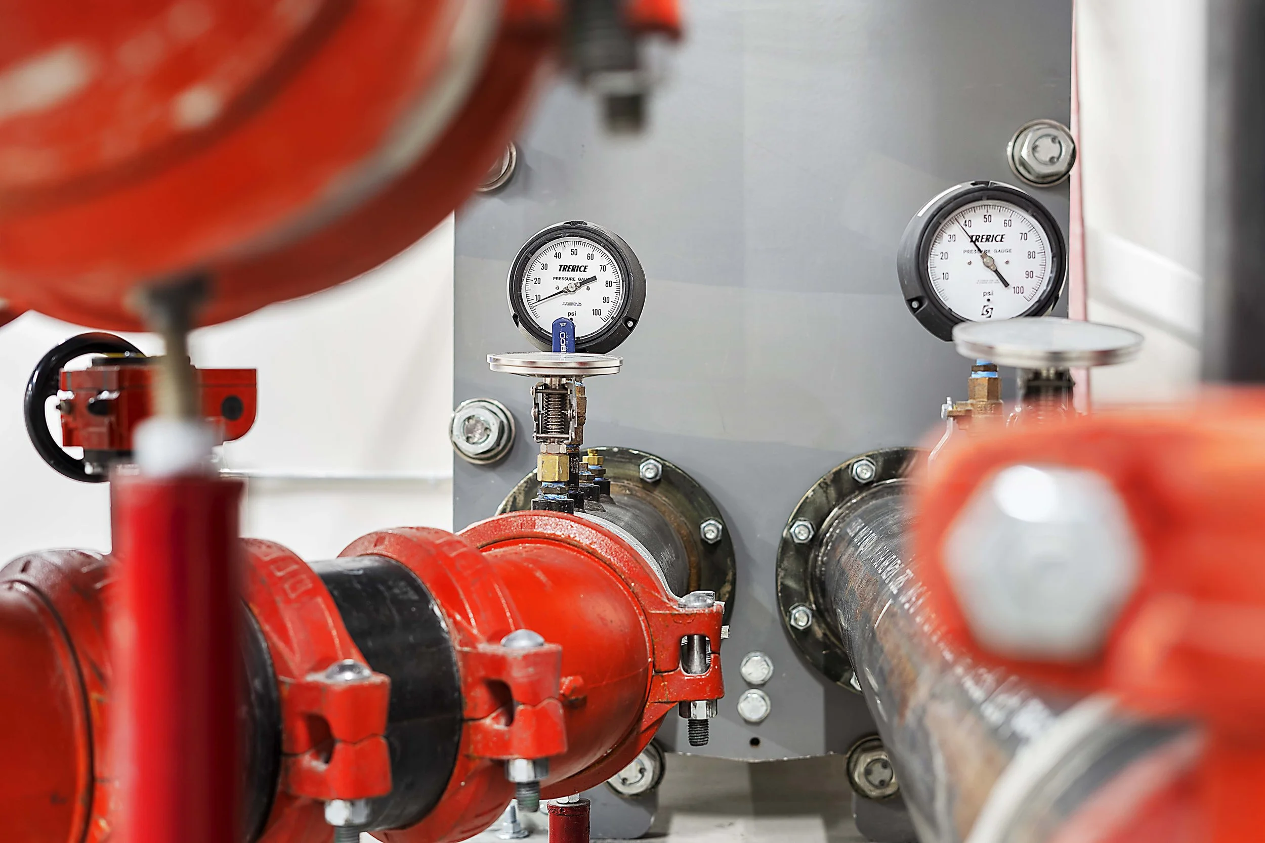 Close-up of industrial plumbing with red pipes, pressure gauges, and a gray metal panel.