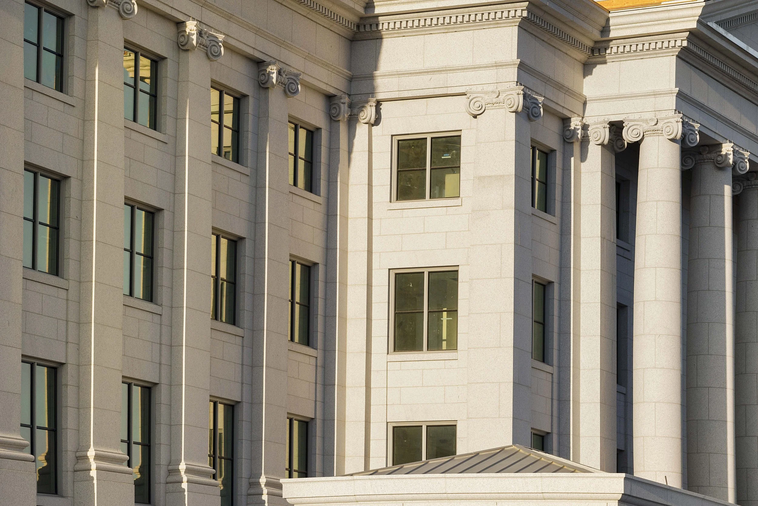 Close-up of a classical building with beige stone facade, columned corners, and multiple rectangular windows.