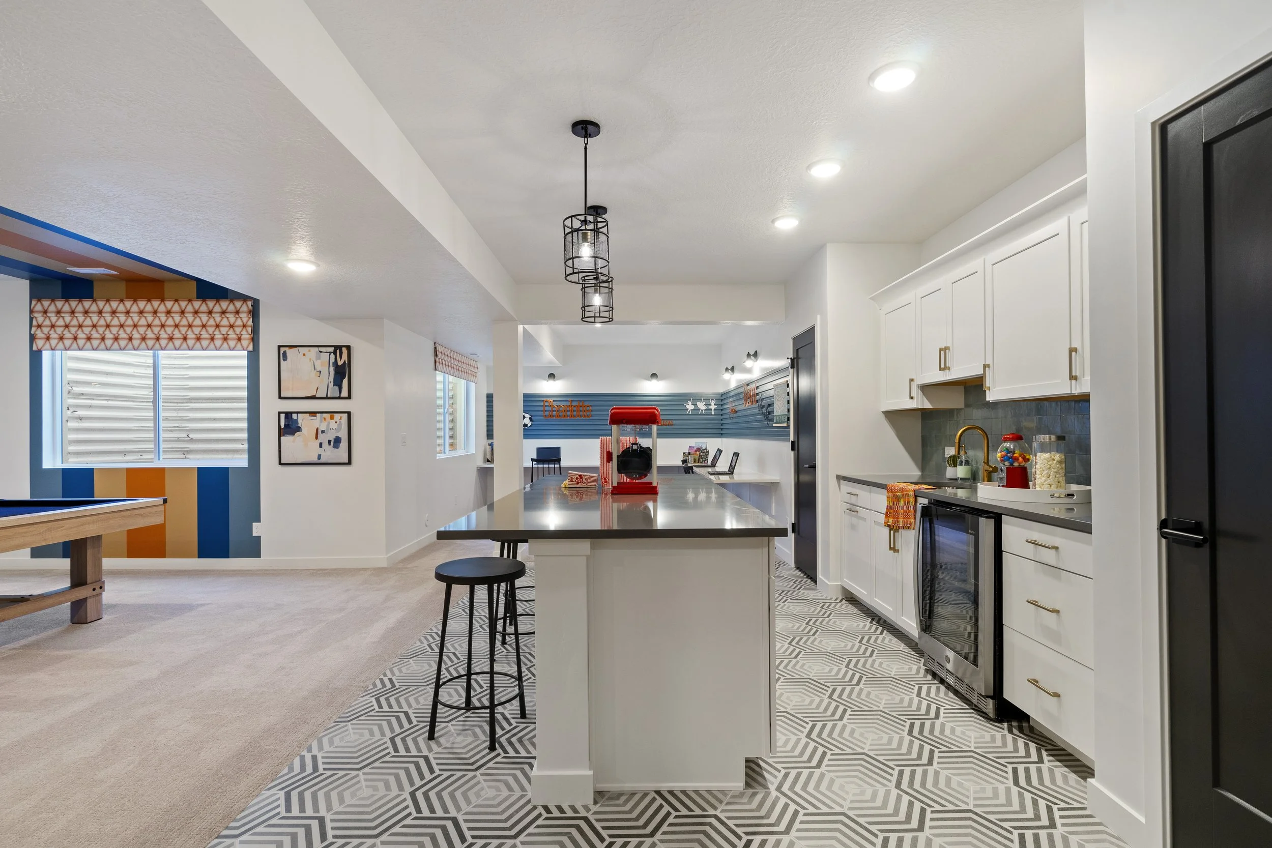 Modern open-concept kitchen with white cabinets, black refrigerator, patterned tile floor, and a central island with a red popcorn maker on top.