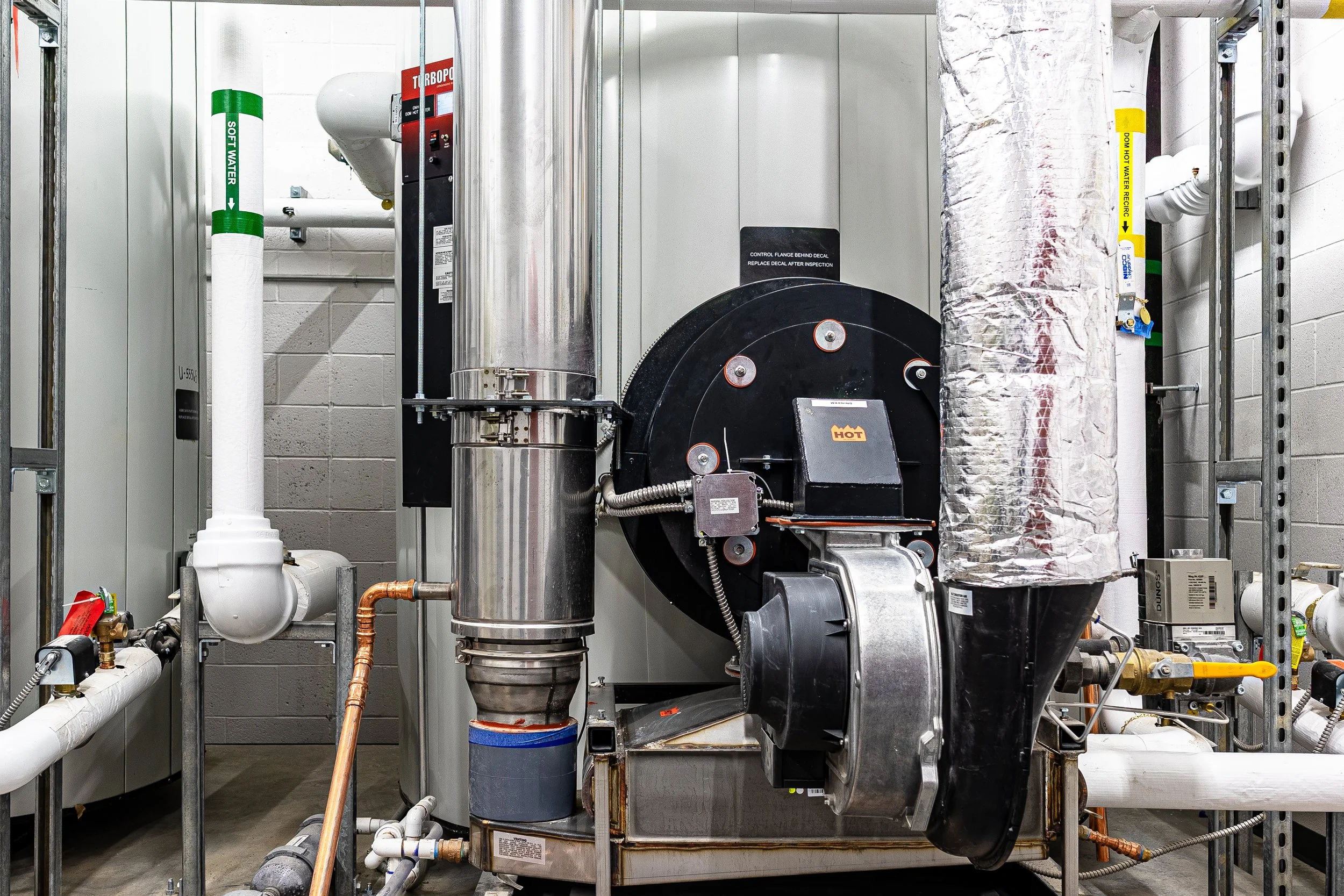Industrial boiler system with pipes, vents, and metal components in a mechanical room.