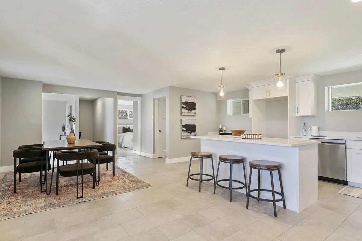Open kitchen and dining area in a home with white cabinets, a kitchen island, bar stools, and a dining table with chairs.