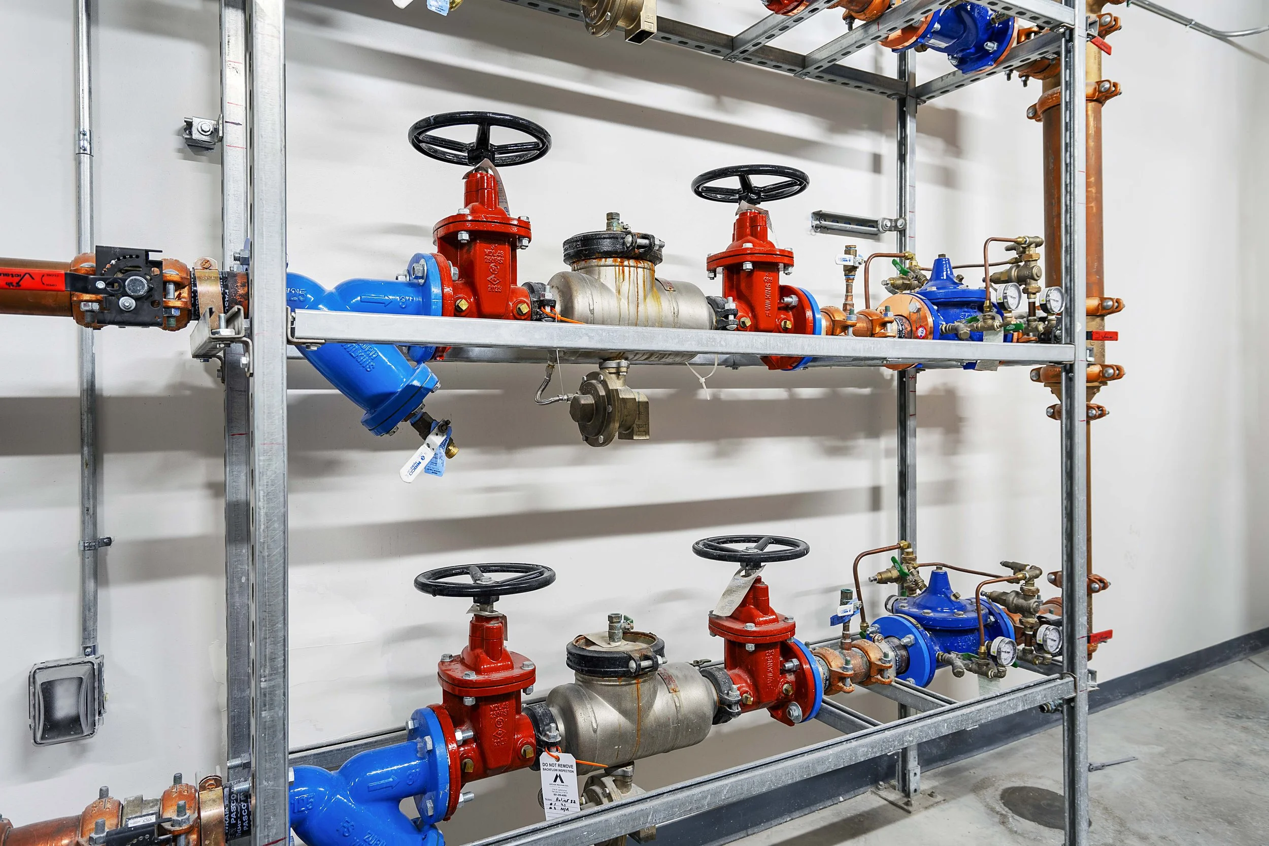 Industrial plumbing system with blue, red, and copper pipes, valves, and gauges mounted on a metal frame.