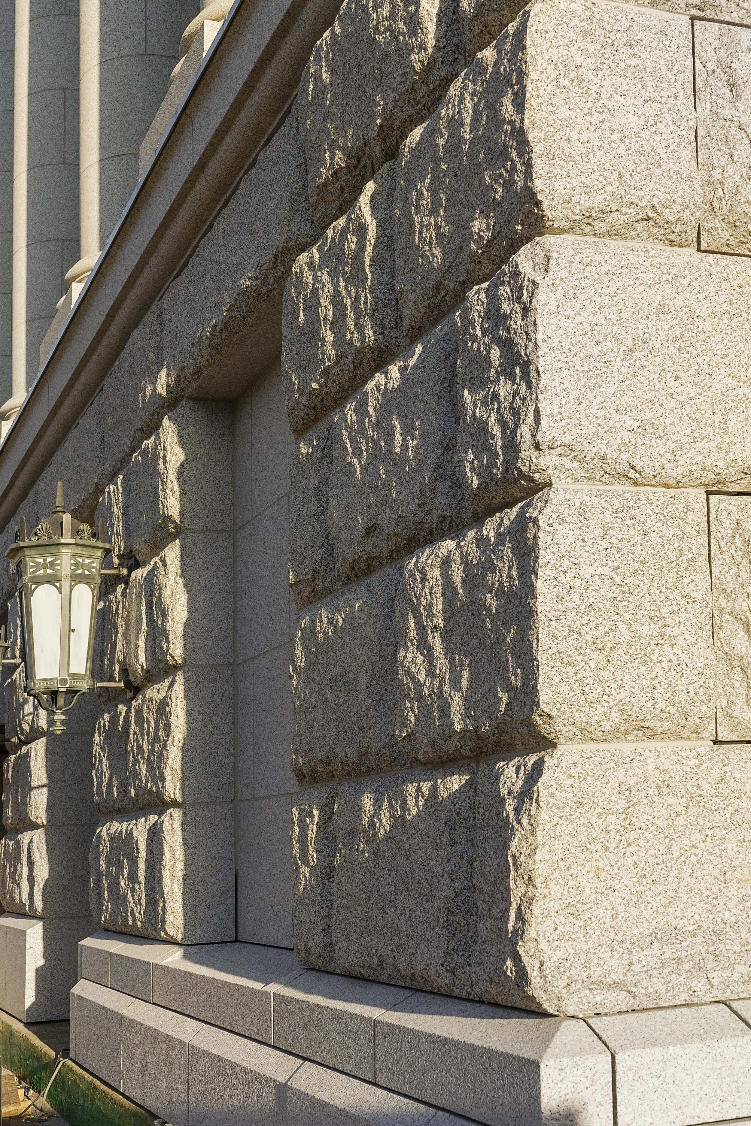 Close-up view of a stone building corner with a decorative outdoor lantern and a shadow cast by the railing above.