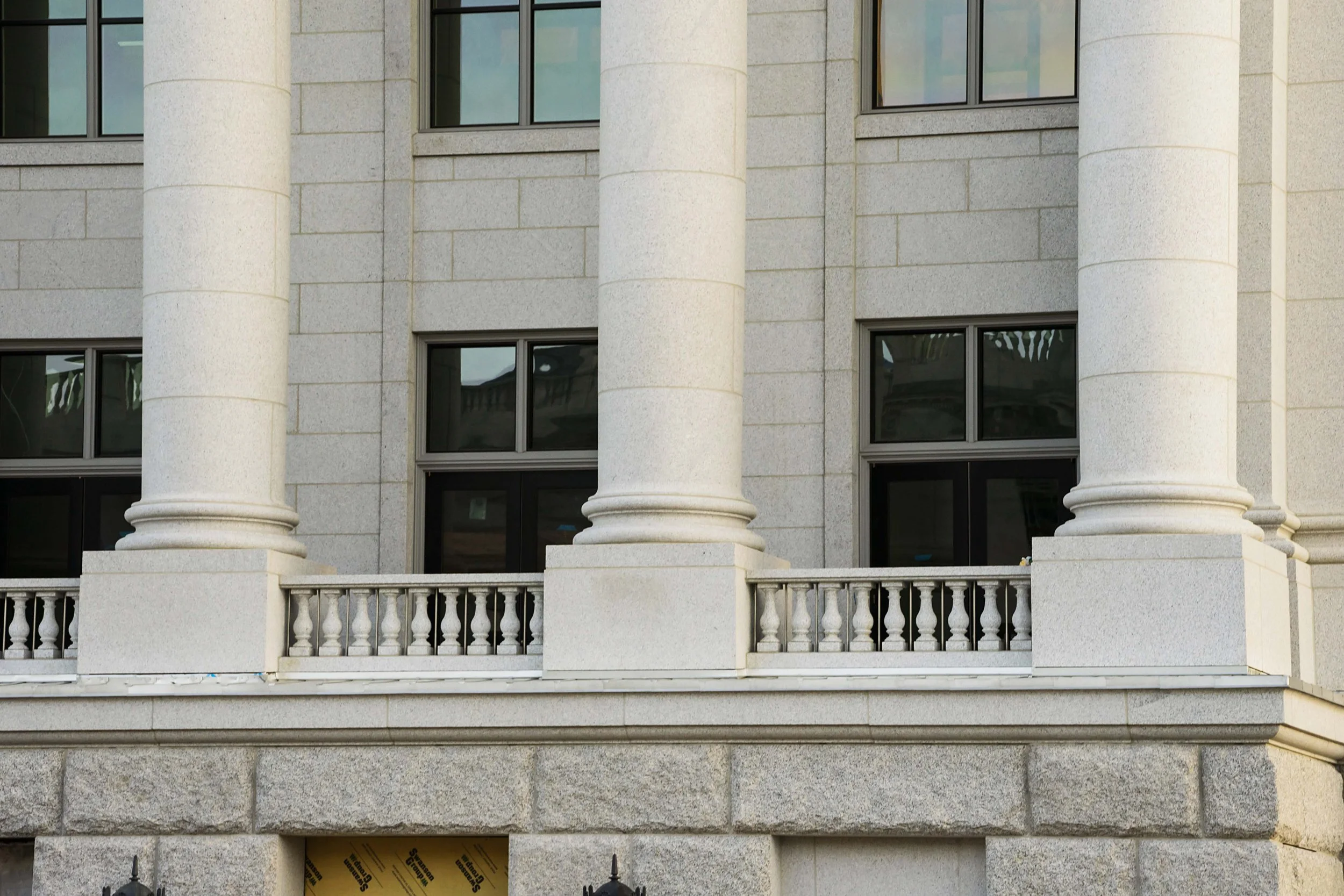 Close-up view of the exterior of a classical-style building with large white columns, granite walls, and black-windowed openings.