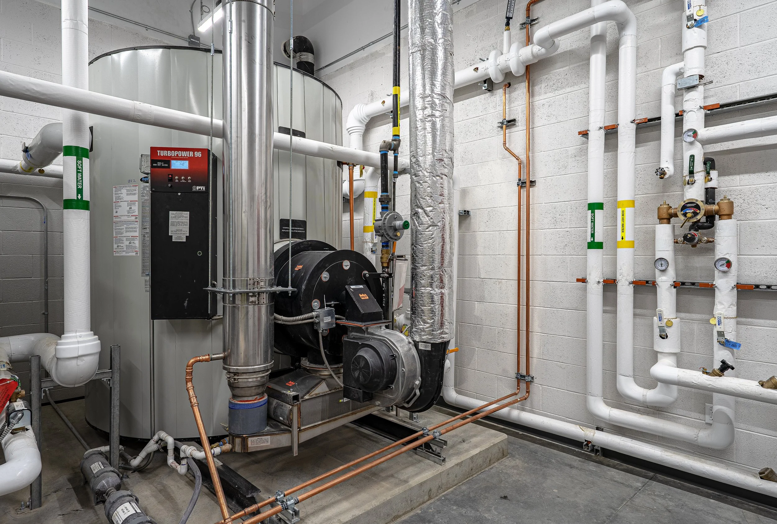 Mechanical room with heating and cooling equipment, including pipes, gauges, and a large black cylindrical component.