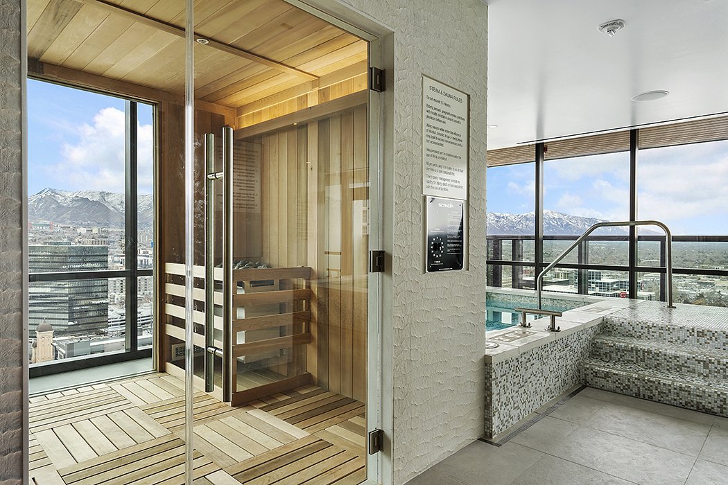 Indoor rooftop pool area with a sauna, large windows showing mountains and city skyline.