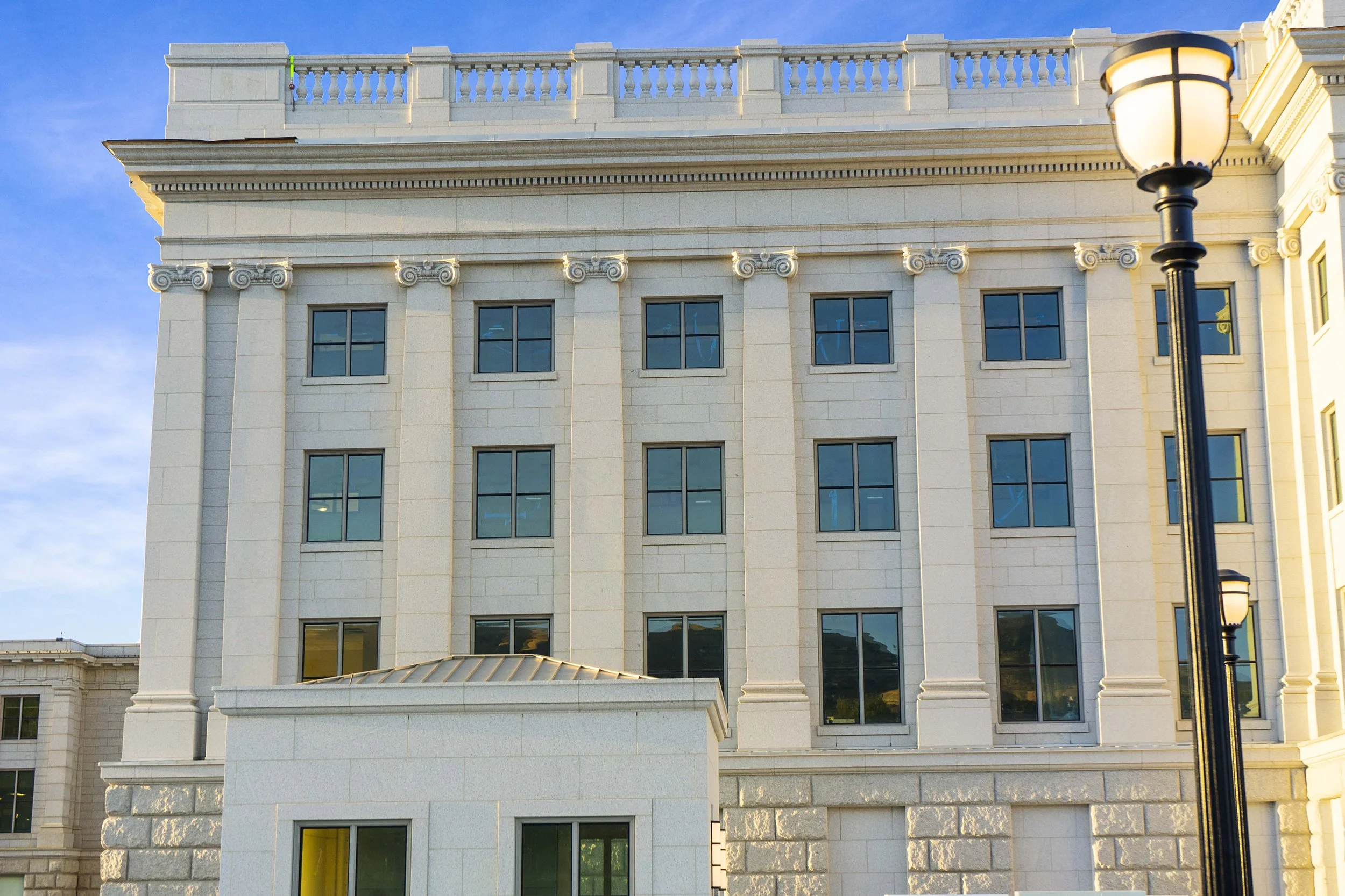 A large multi-story building with cream-colored stone facade, symmetrical windows, ornate decorative elements, and a topped rooftop terrace with a balustrade, illuminated by a streetlamp in the foreground.
