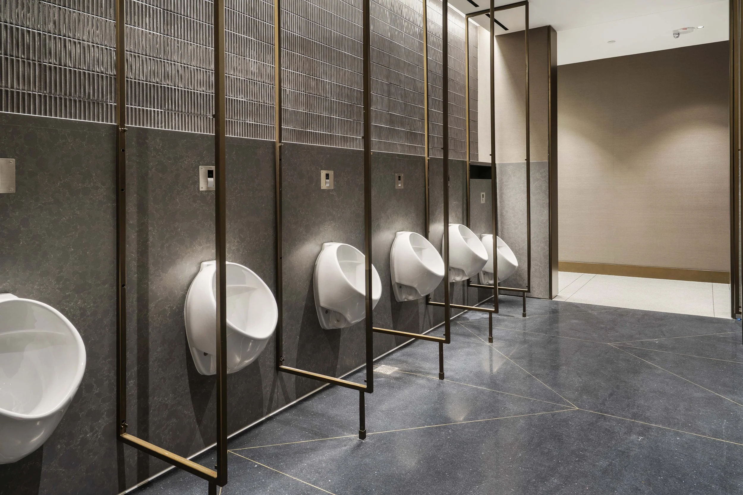 A row of five white urinals mounted on a dark wall with modern decor in a men's public restroom.