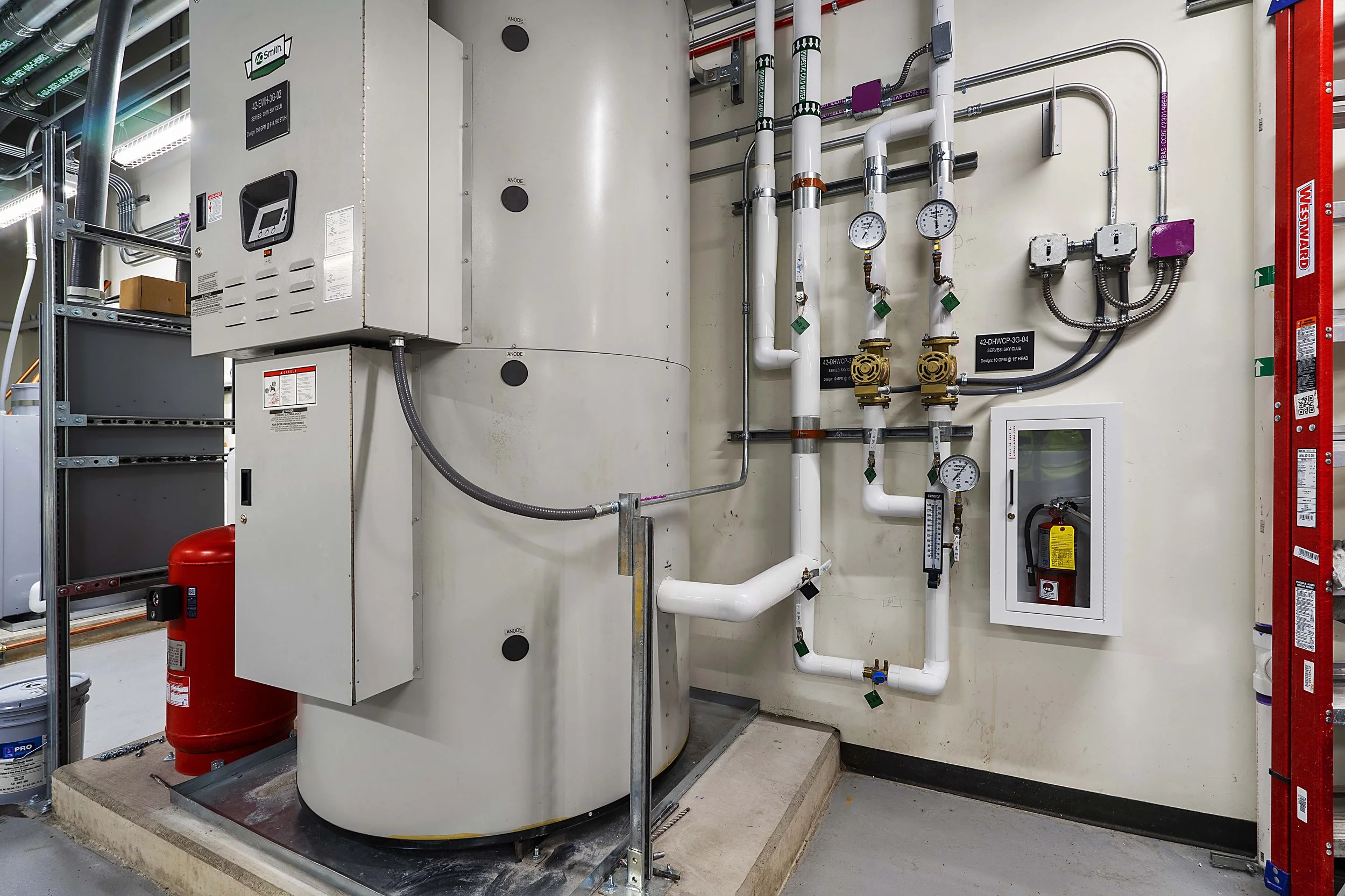 Mechanical room with pipes, gauges, electrical panels, and a fire extinguisher.