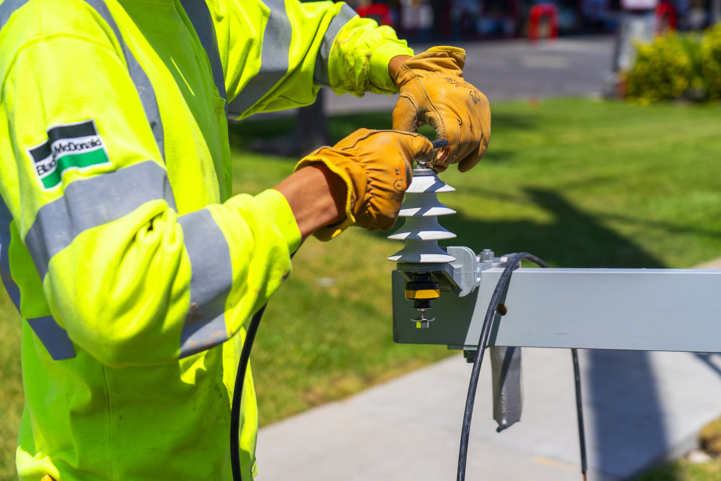 Worker in high-visibility safety jacket and gloves installing or repairing electrical equipment on a street pole.