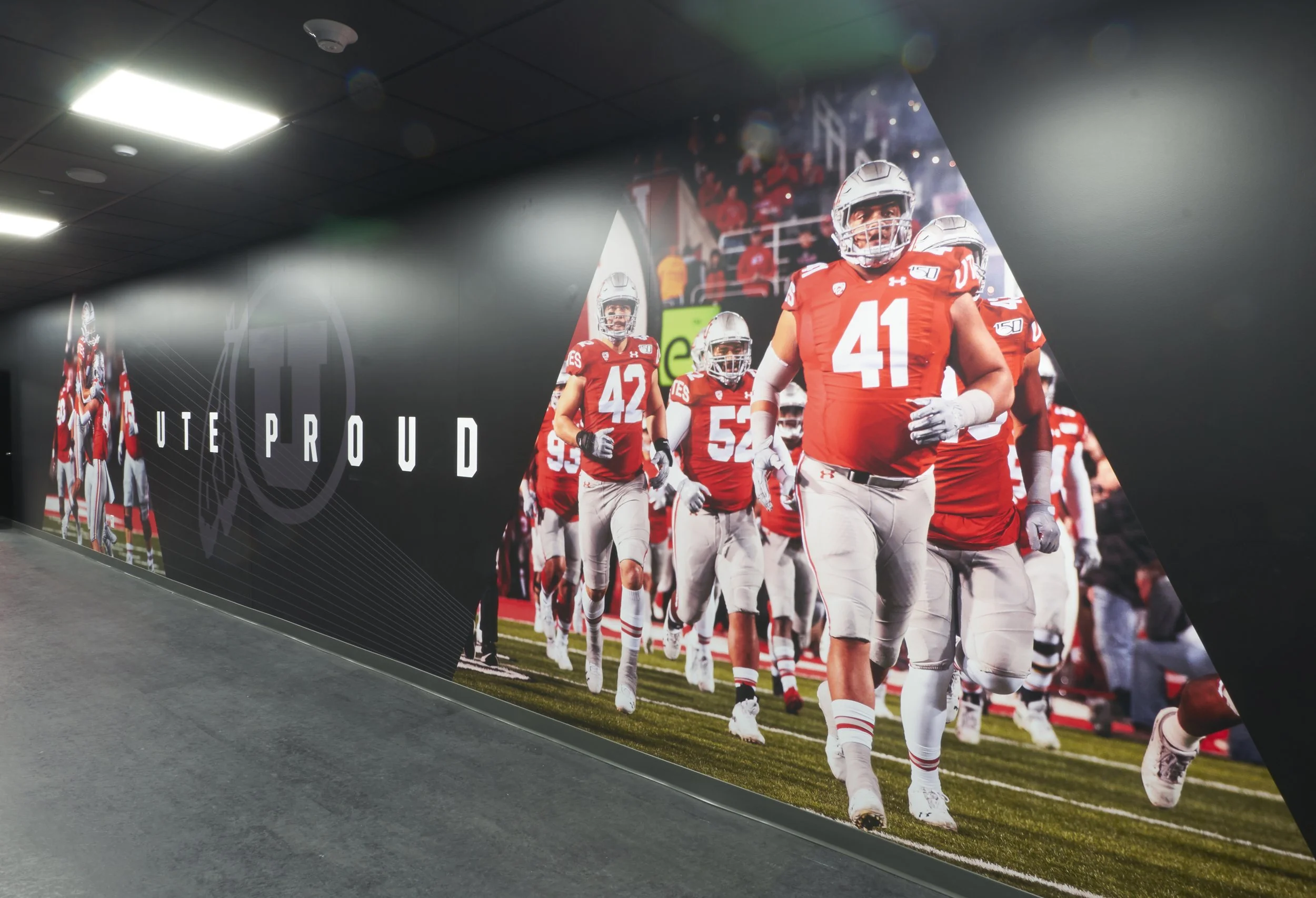 A large wall mural showing football players in red and white uniforms running onto the field with a crowd in the background. The phrase 'UTE PROUD' is written on the wall.