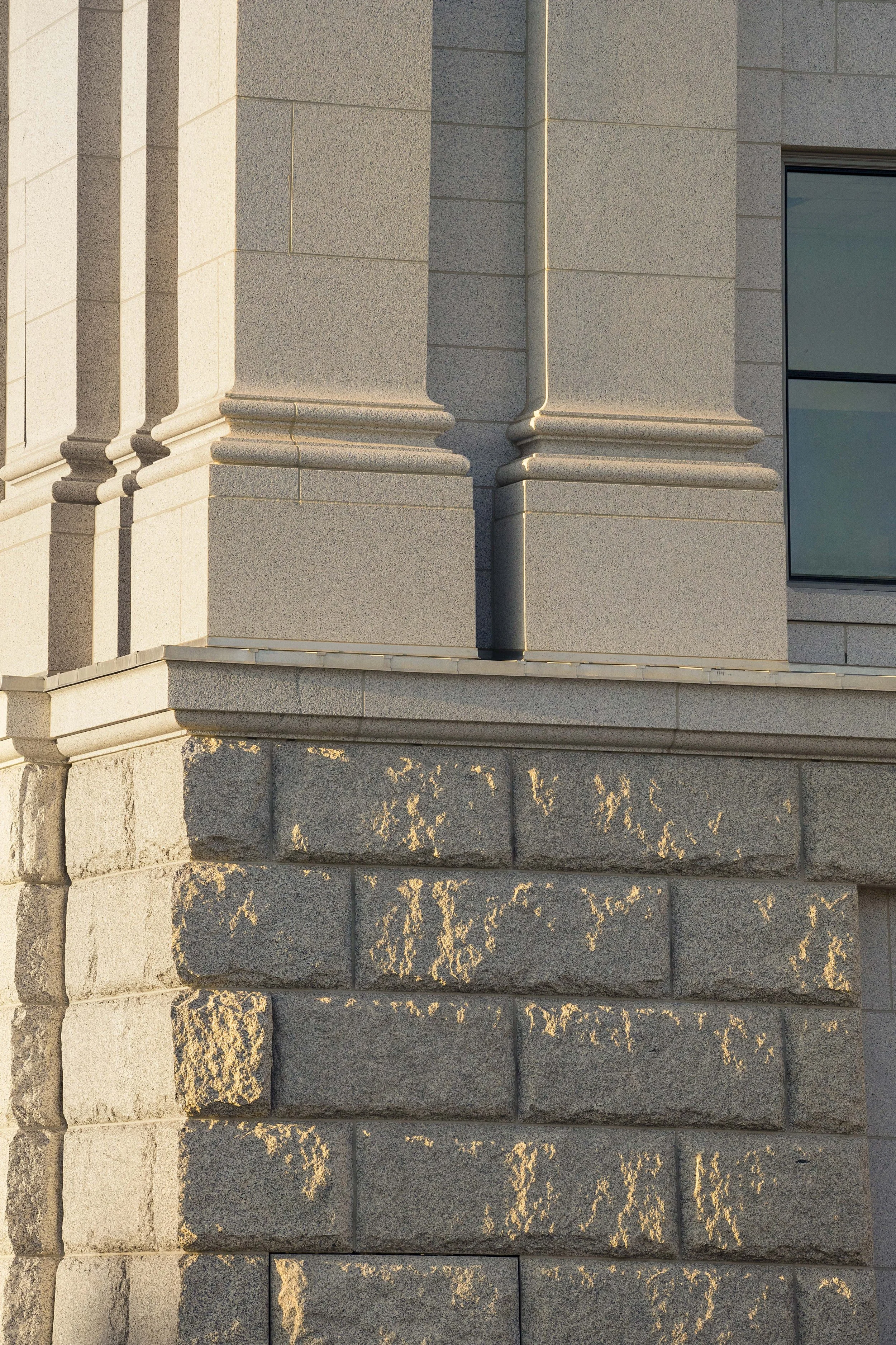 Close-up of a building corner with stone and concrete architecture, including decorative cornices and a large window.