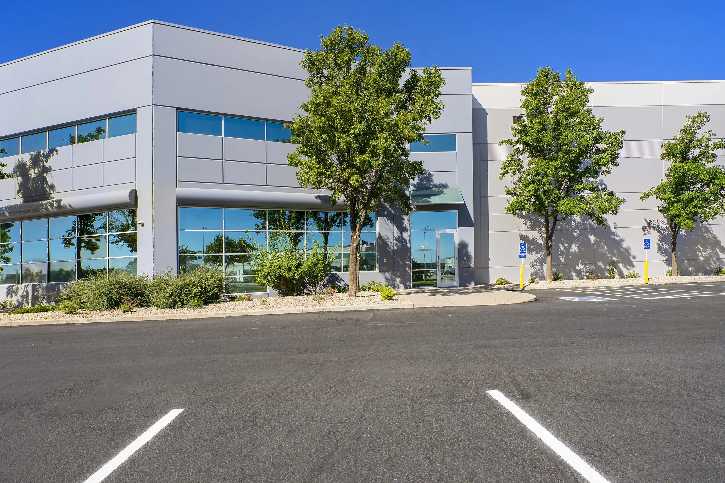 Modern office building with glass windows, trees, and a parking lot with marked spaces and handicapped parking signs.