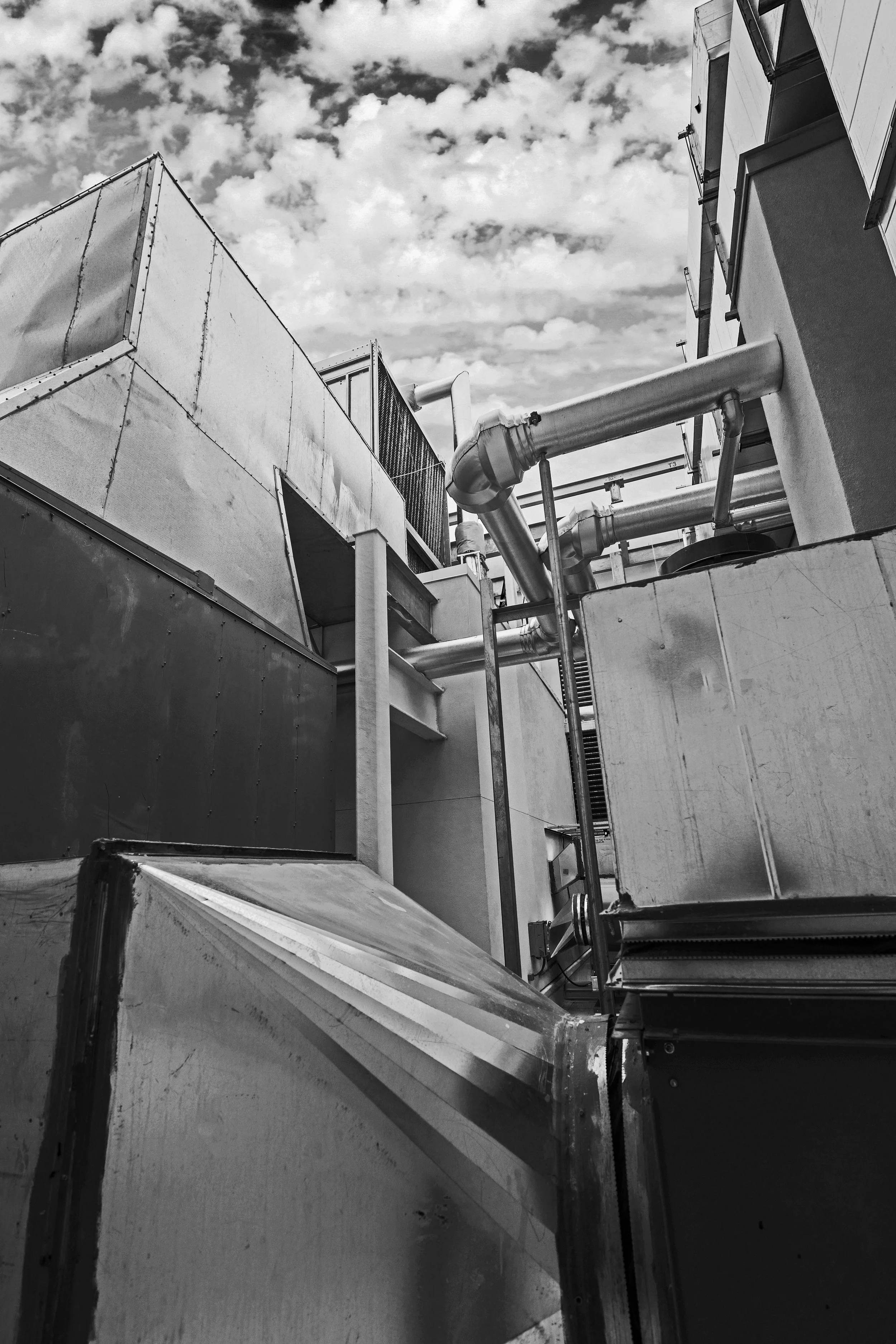 Black and white photo of industrial rooftops and pipes against a cloudy sky.