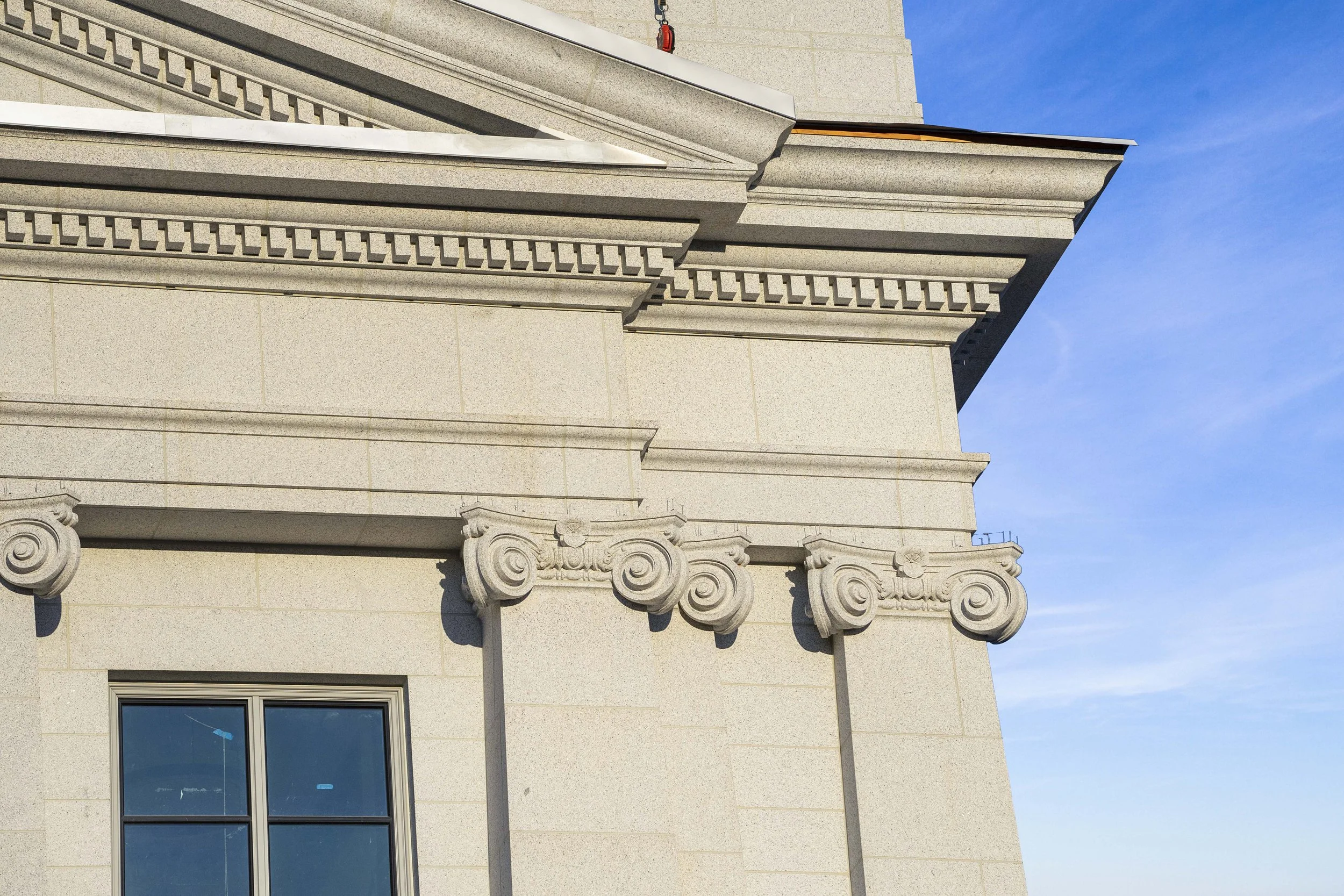 Close-up of beige stone building corner with decorative architectural details, window, and blue sky in background.