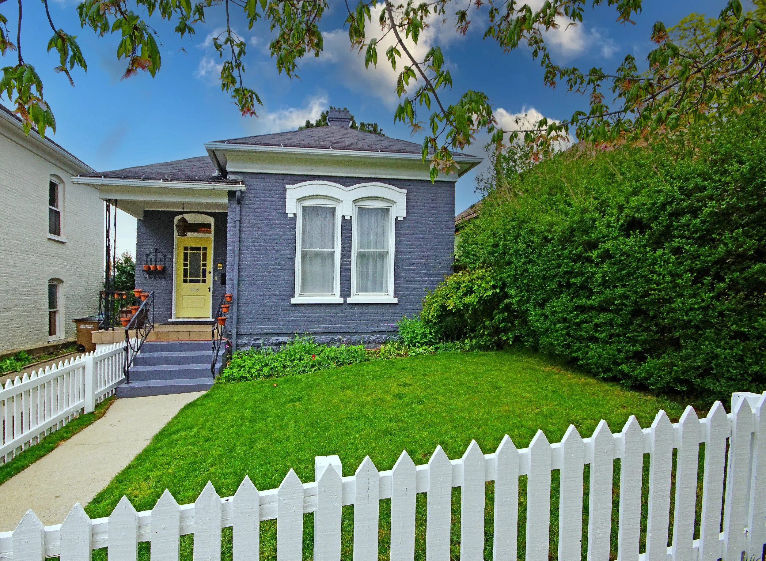 Small blue house with white trim, front porch, white picket fence, and green lawn.
