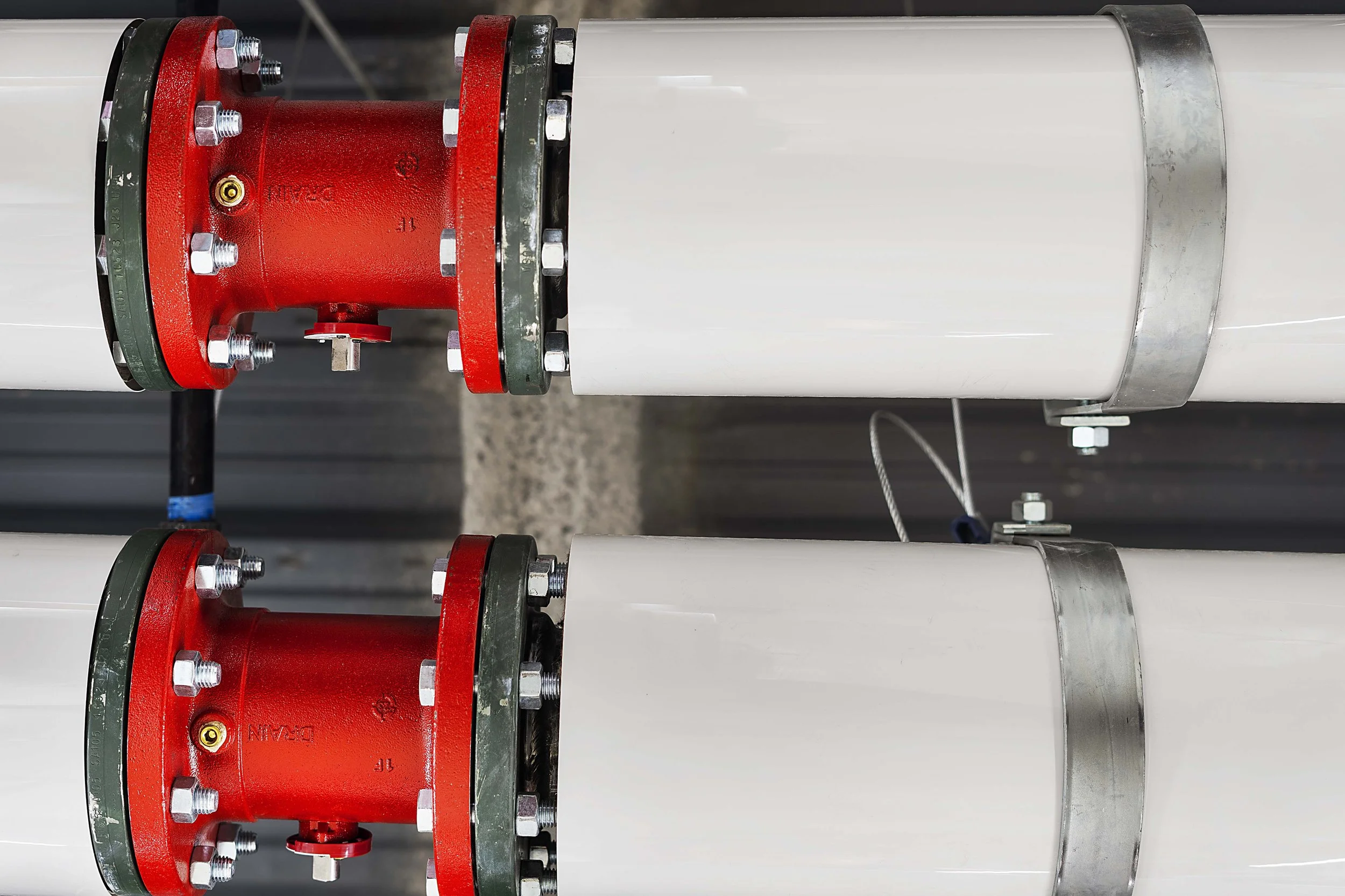 Close-up view of two white underground pipes connected with red and green flanged fittings, secured with bolts, in an industrial setting.