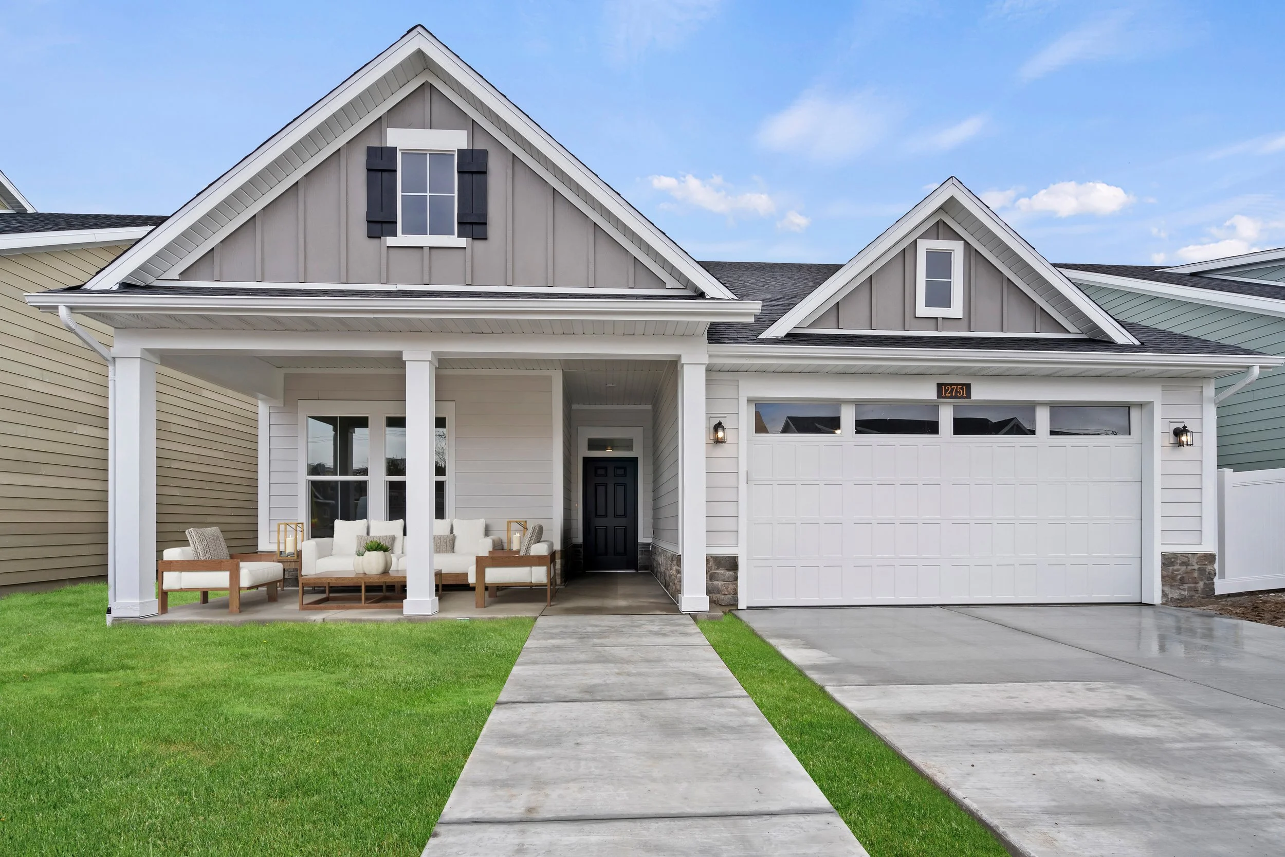 Modern suburban house with a gray gabled roof, white exterior, front porch with furniture, and attached garage.