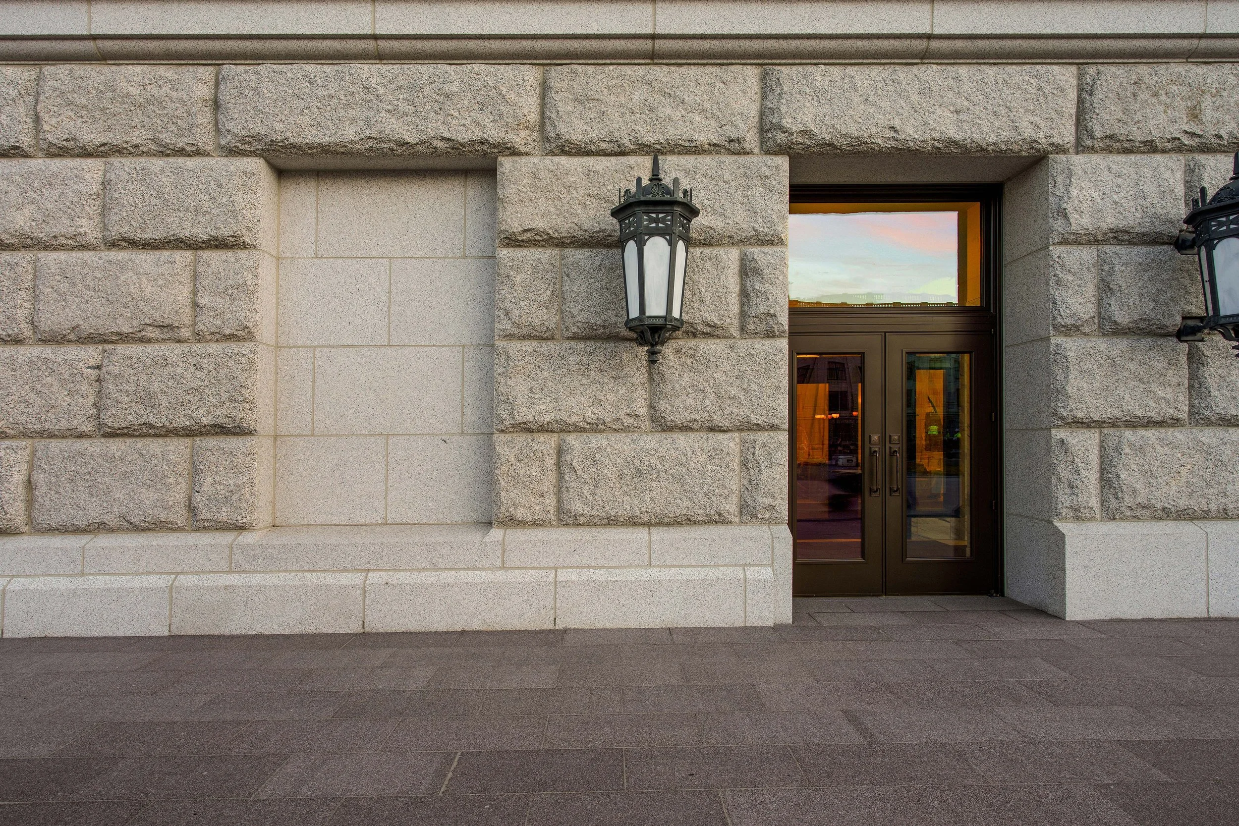 Exterior view of a building with a large stone brick wall, a glass door, and decorative black lantern-style wall sconces.