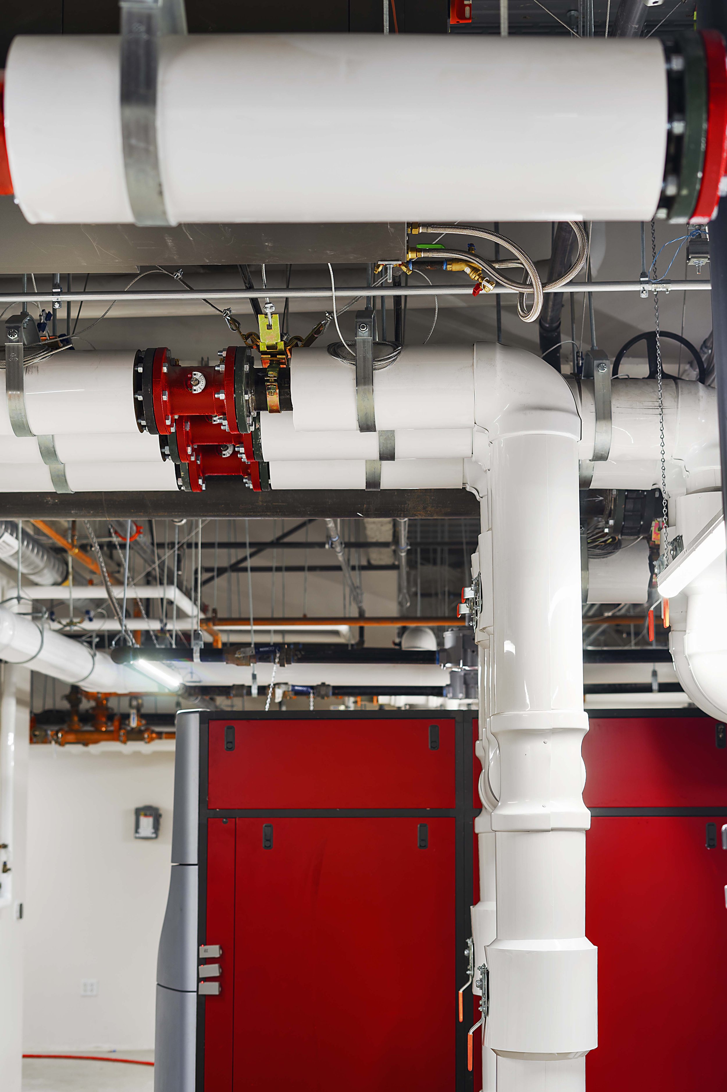 Industrial plumbing with white pipes, red valve fittings, and a large red cabinet in an industrial or mechanical room.