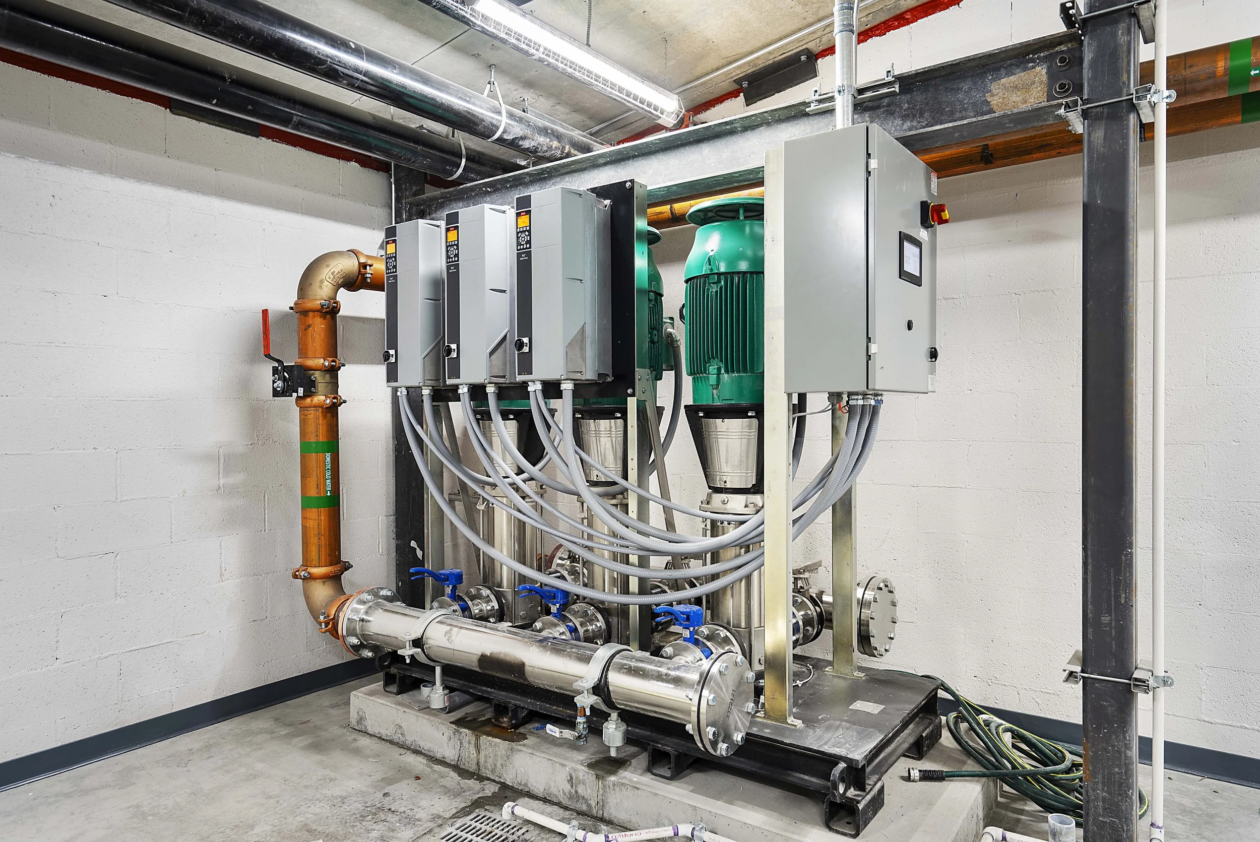 Industrial mechanical equipment consisting of green motors, metal pipes, and control boxes mounted on a concrete platform in a utility room.