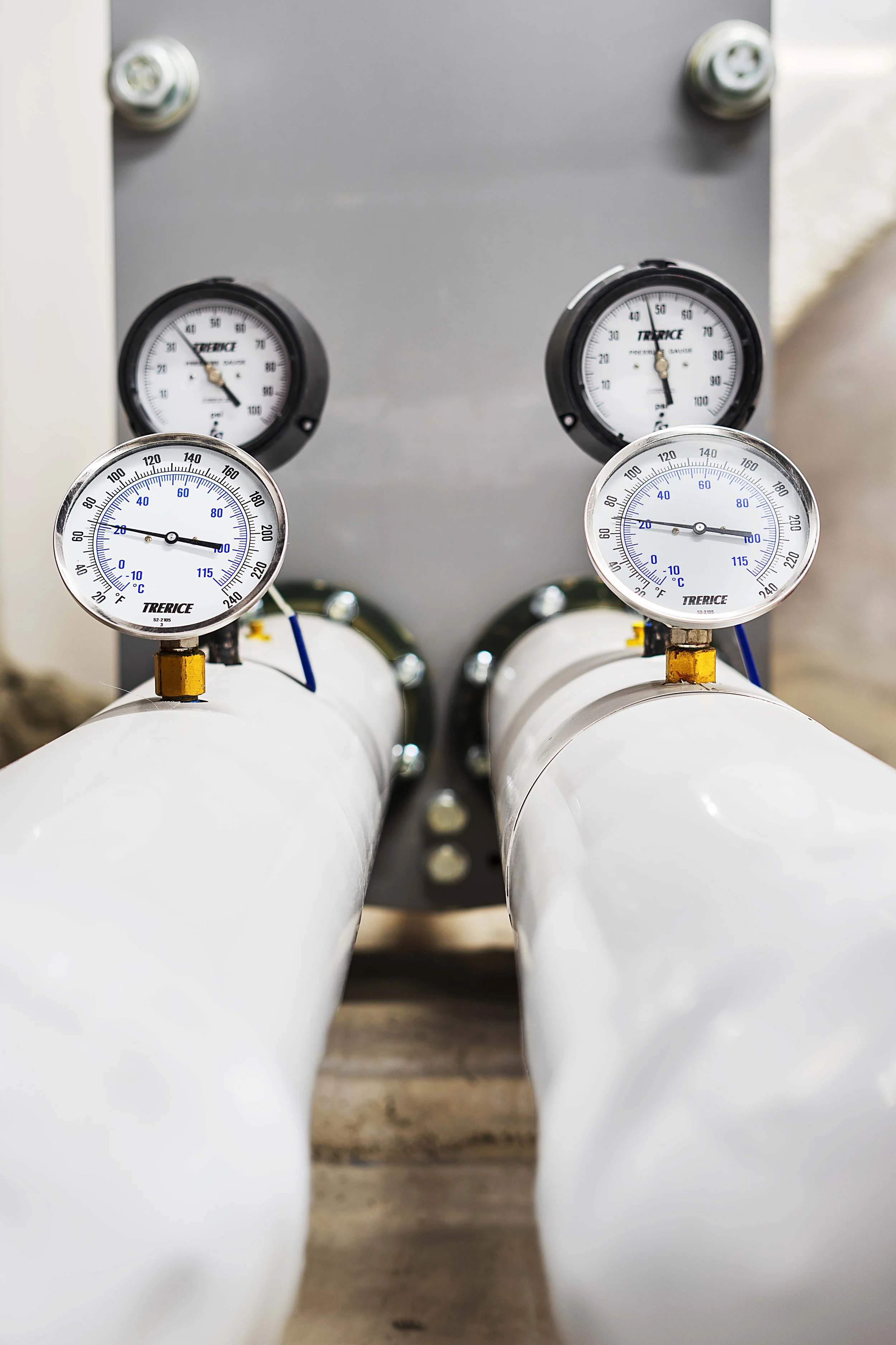 Two white pipes with pressure gauges attached, installed against a gray background.