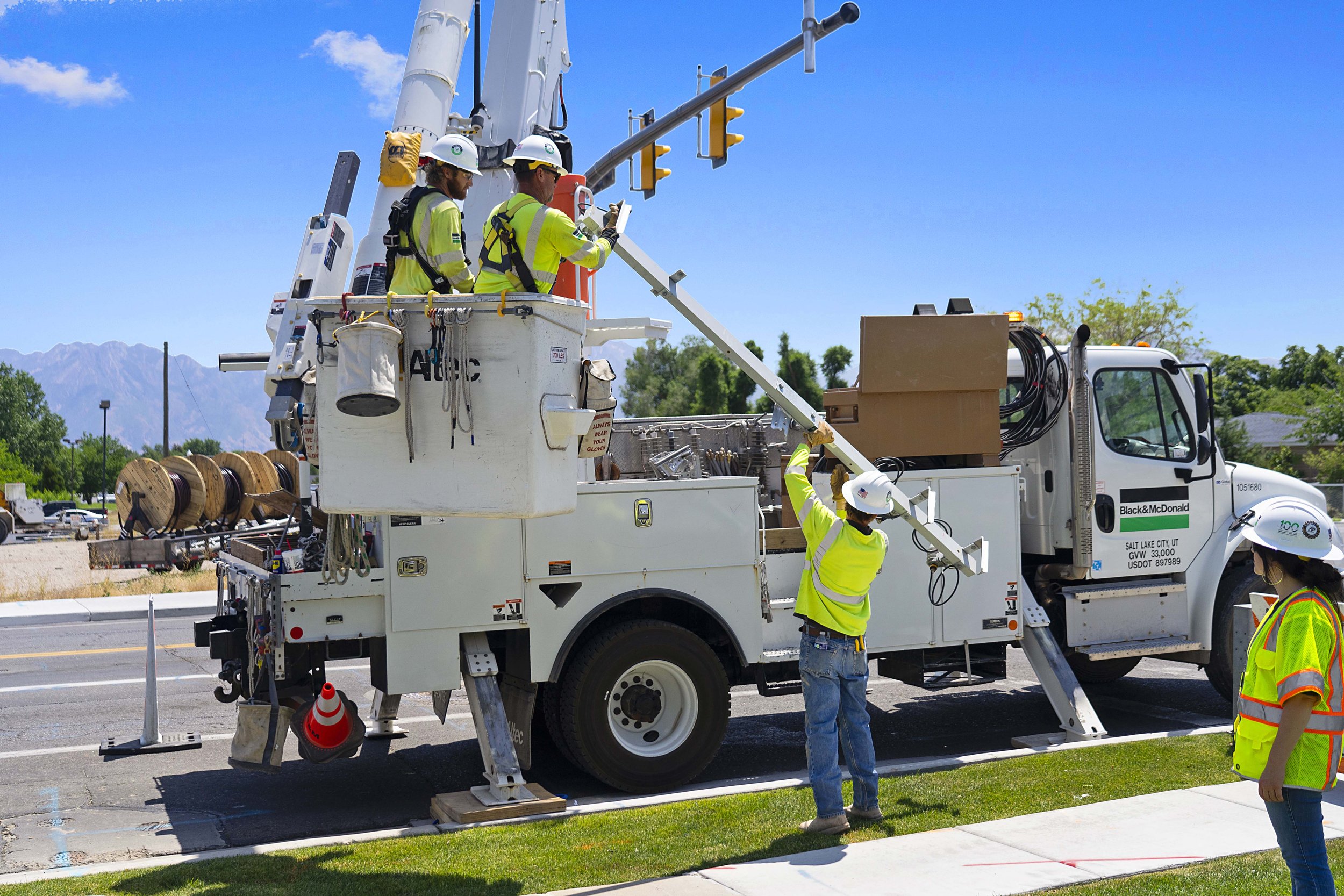 Workers in safety gear repairing traffic lights using a bucket truck on a sunny day.
