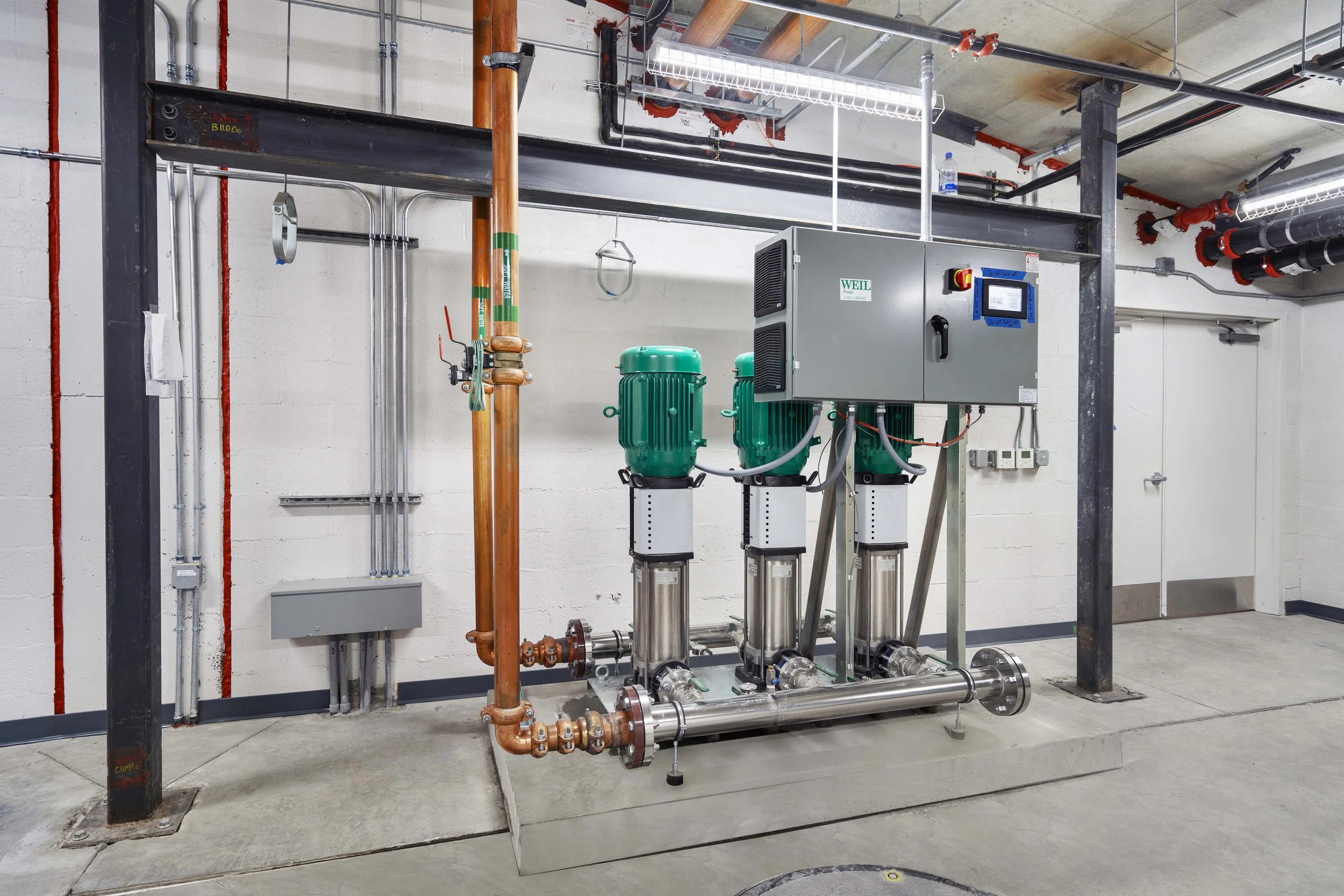 Industrial mechanical equipment including pumps, pipes, and control panel in utility room