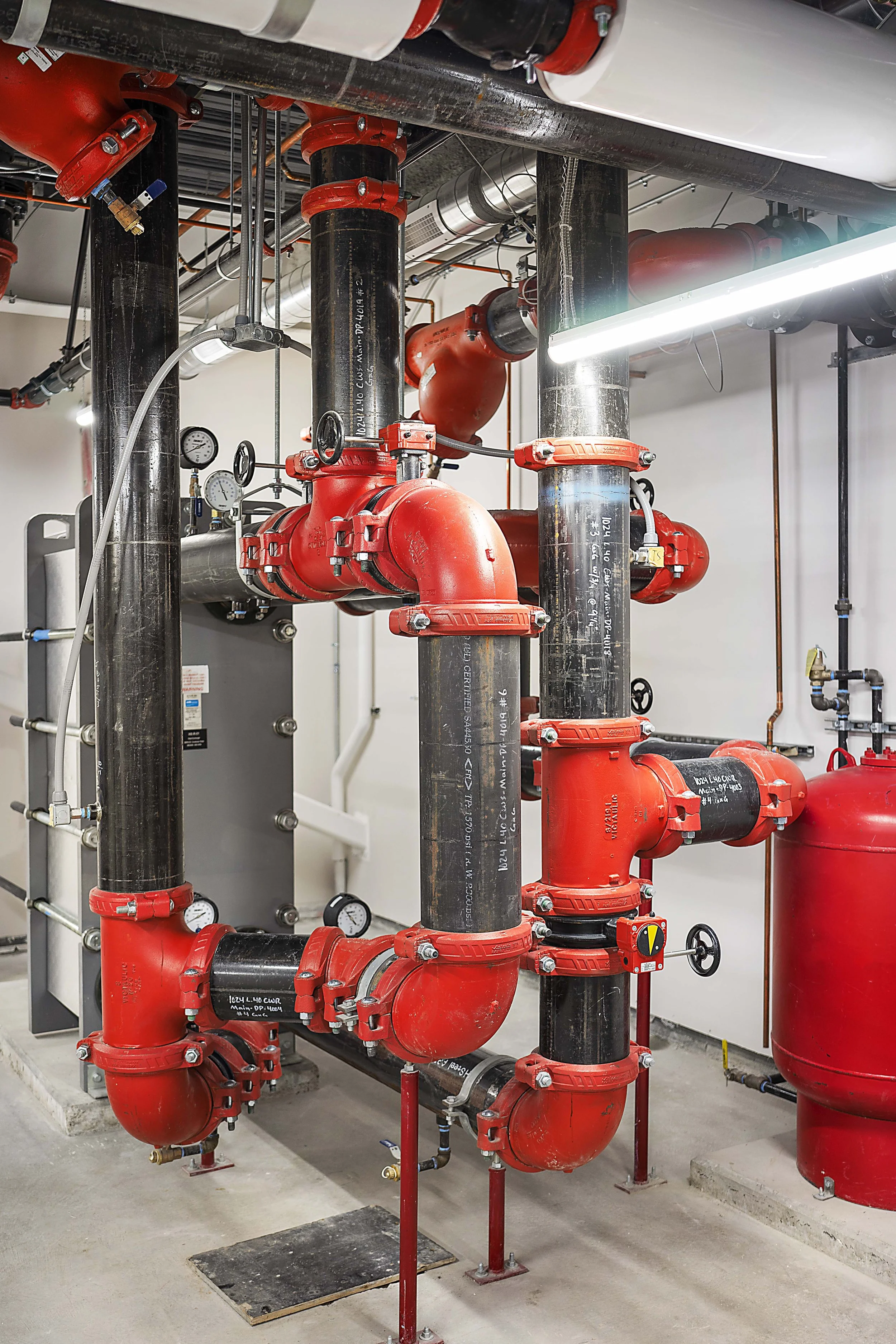 An industrial mechanical room with black and red pipes, gauges, and valves.