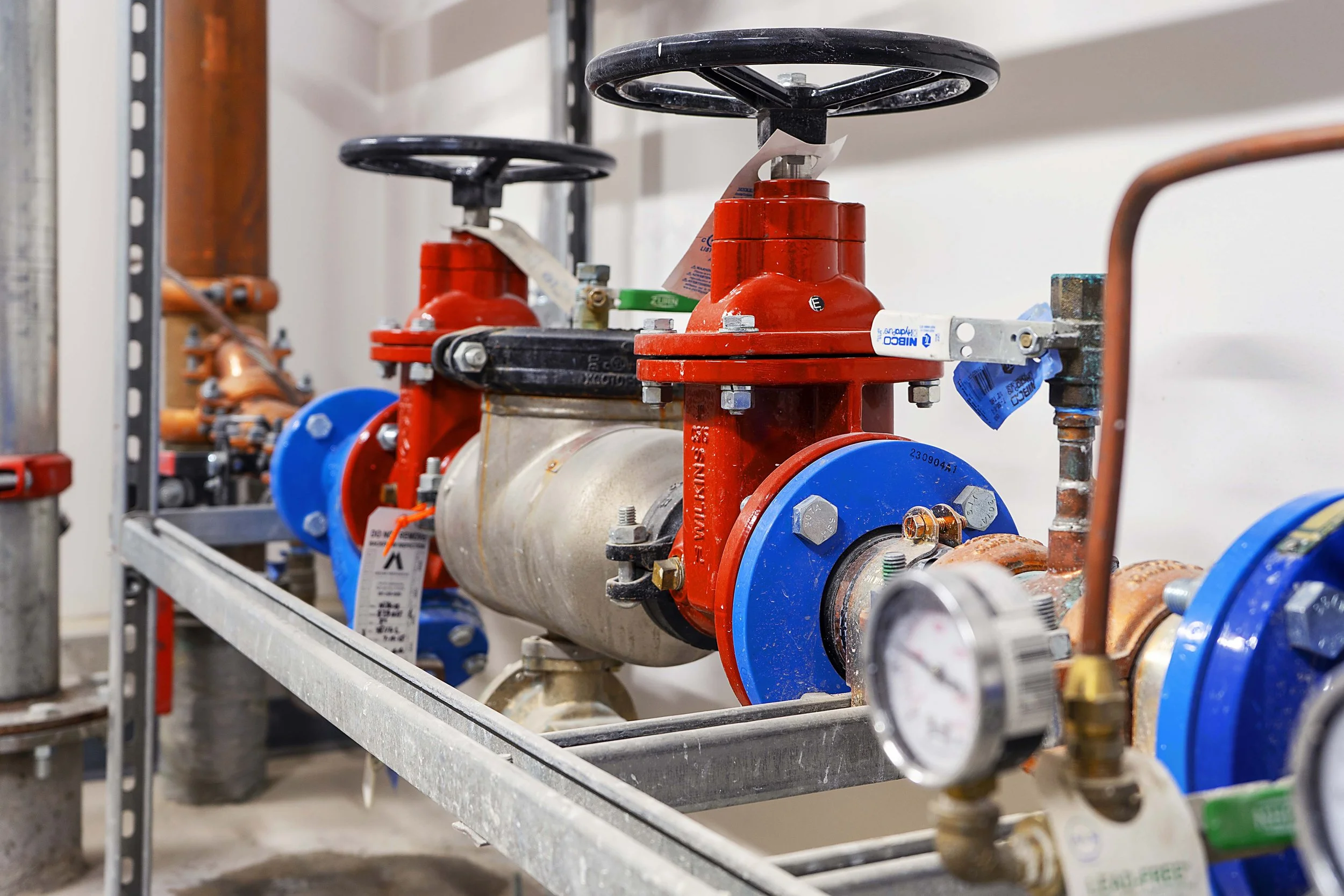 Industrial plumbing system with red and blue valves, pipes, and gauges on a metal frame.