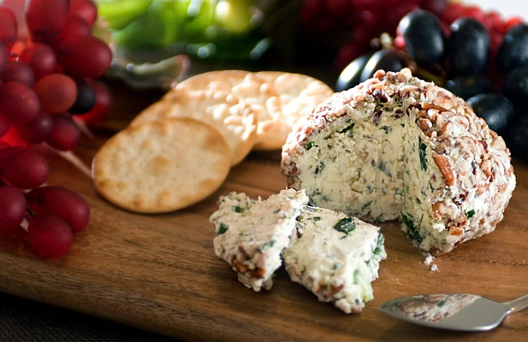 Cheese ball on a wooden platter with crackers and grapes.