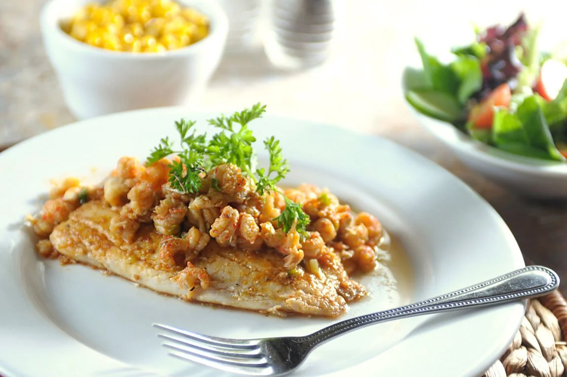 Plate of fish topped with shrimp and herbs, with sides of corn and salad.