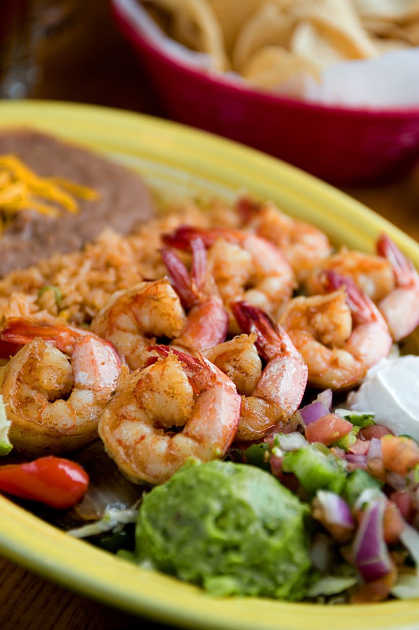 Mexican shrimp dish with rice, refried beans, guacamole, and pico de gallo on a yellow plate.