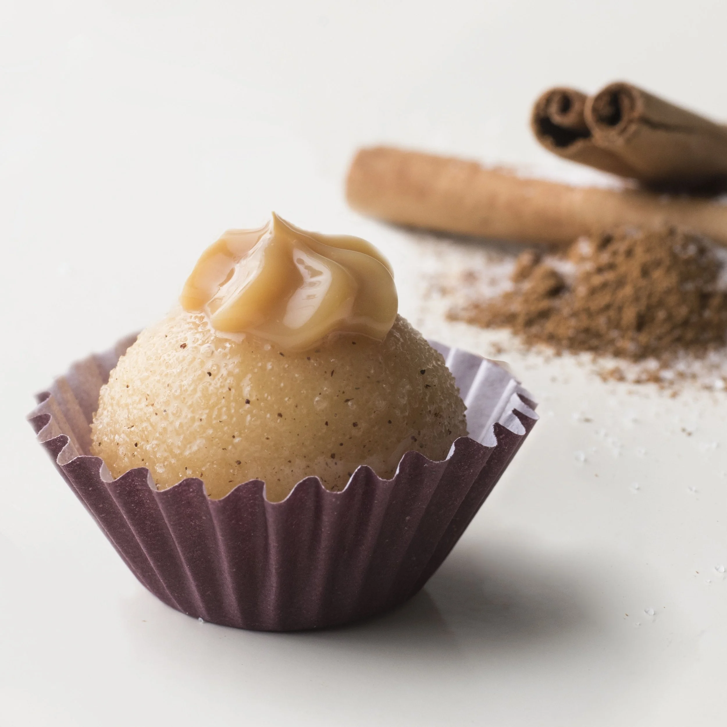 Brigadeiro with cinnamon flavor in a paper cup, topped with creamy caramel, with cinnamon sticks and ground cinnamon in the background.