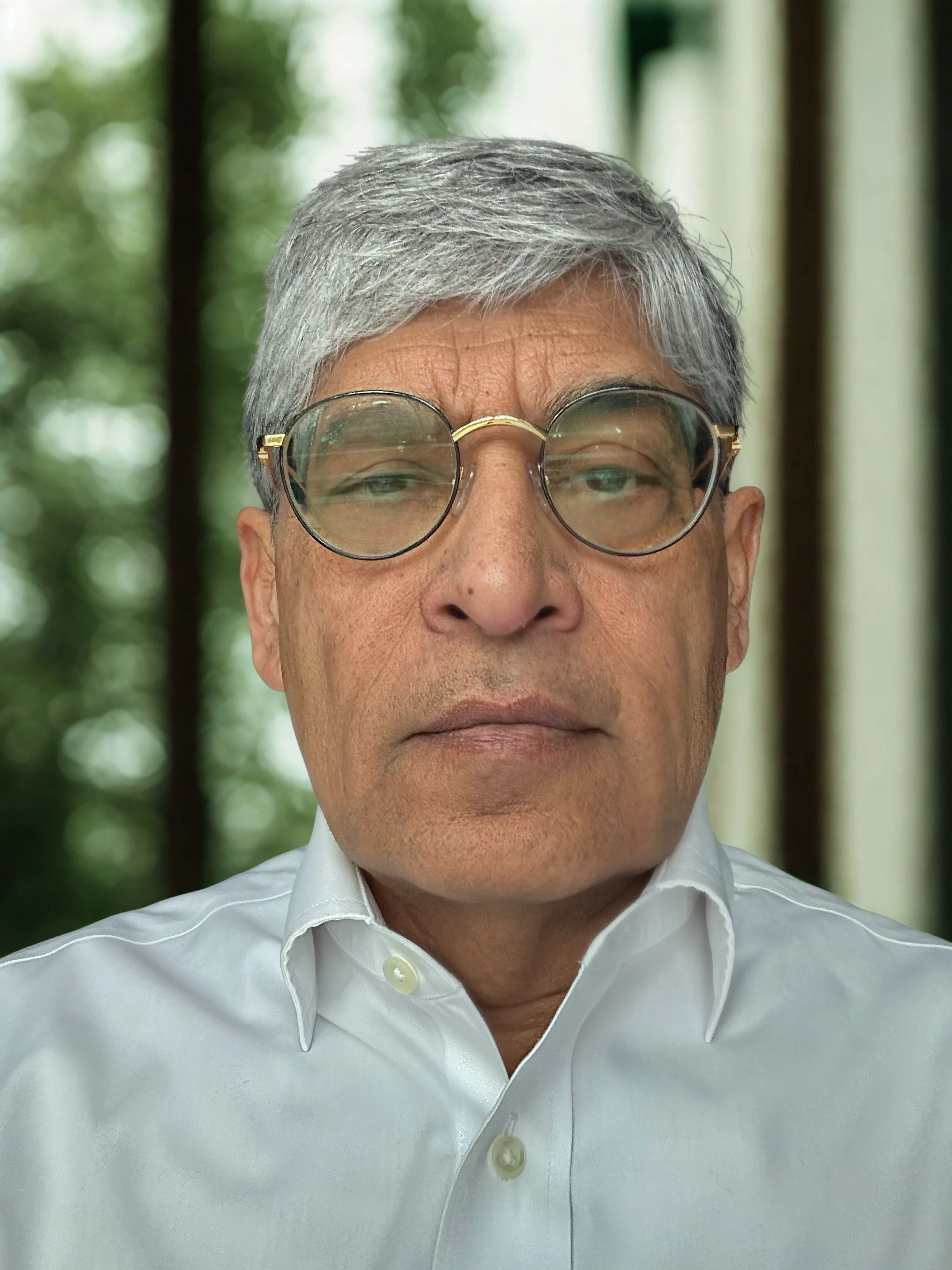 Stack of three books with a pair of eyeglasses on top, seen on a surface with a blurred yellow pillow in the background.
