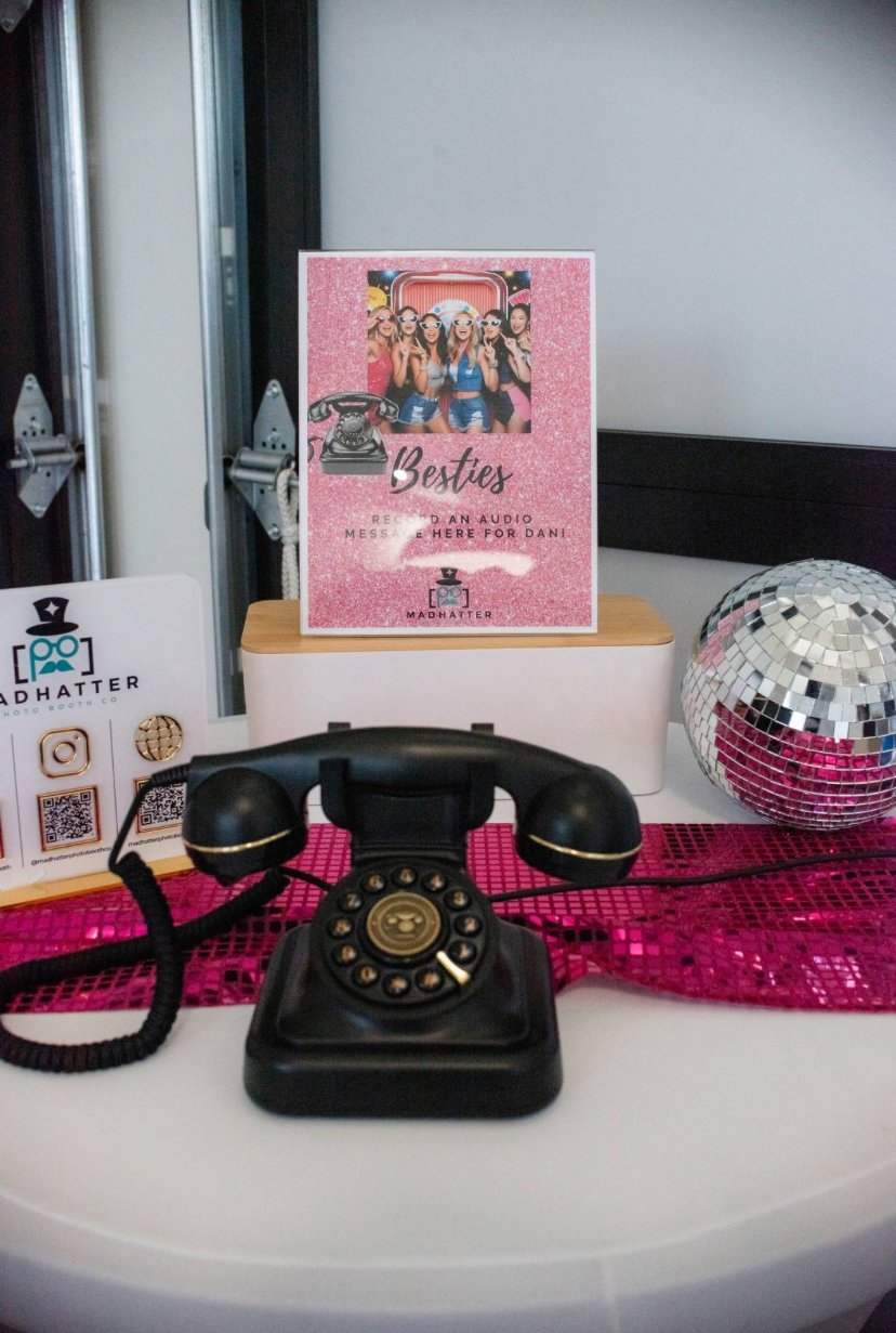 Black vintage rotary telephone on a white table with floral and plant decor in the background.
