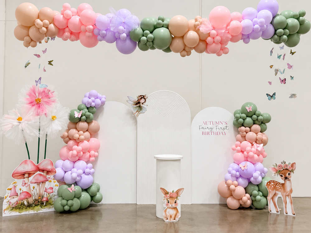 Decorative pastel balloon arrangement with clouds and sprinkles, featuring a large donut balloon for a birthday celebration, with a white backdrop that says 'Kaileah's Sweet One' for a first birthday party.
