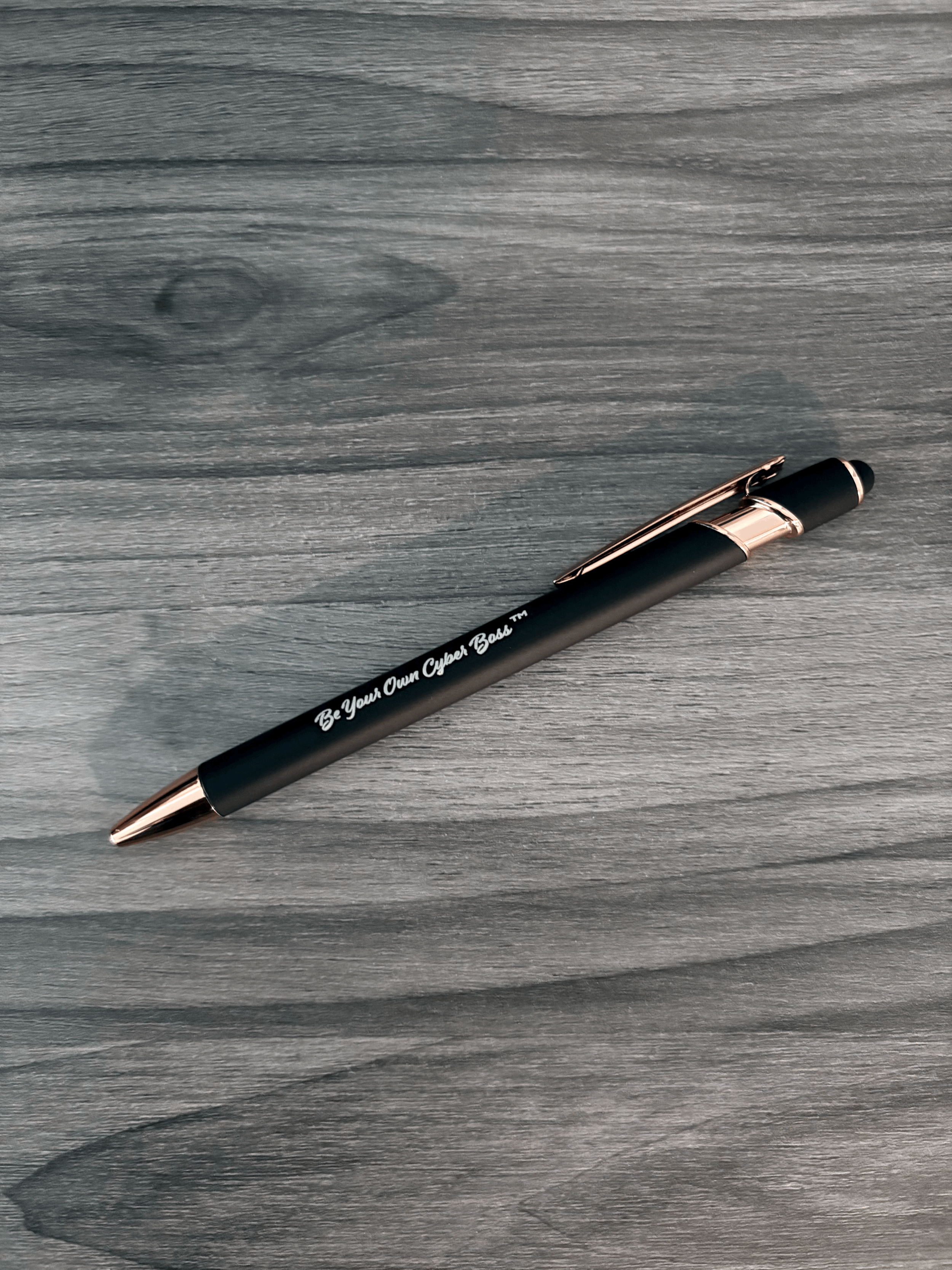 Black Cyber Boss™ ballpoint pen with rose-gold trim and ‘Be Your Own Cyber Boss™’ text displayed on a wood surface.